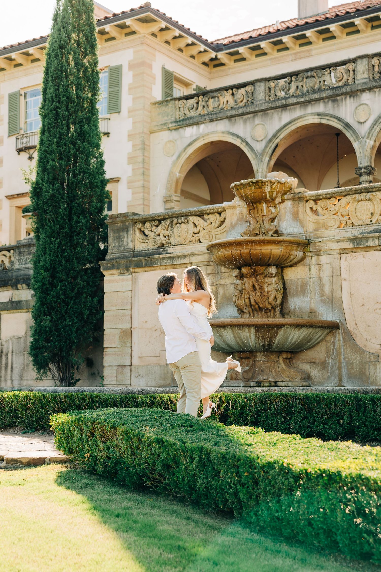 Elegant Mediterranean villa with cypress trees and manicured gardens features ornate architectural details and stone facade.