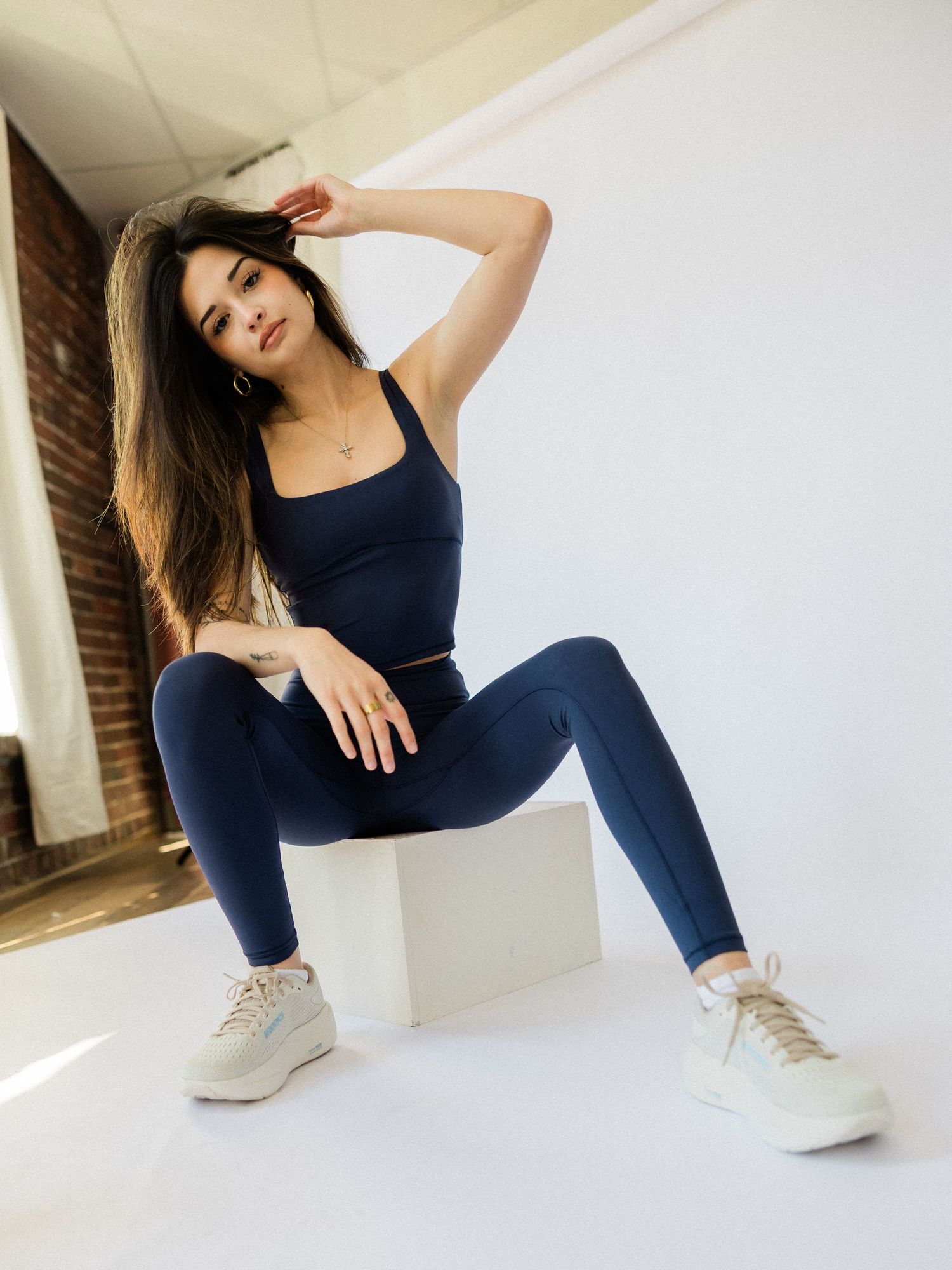 A woman in navy workout attire strikes dynamic poses against a white wall in a four-photo collage sequence.
