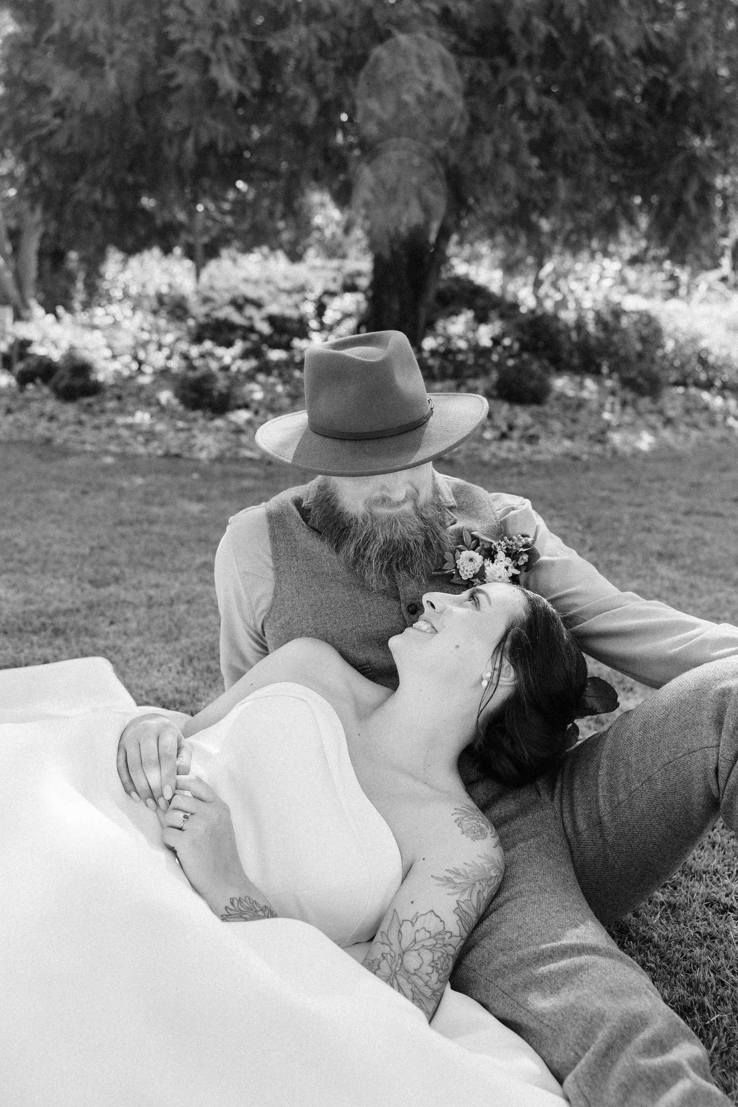 Intimate black and white portrait of newlyweds resting together on grass during their wedding day.