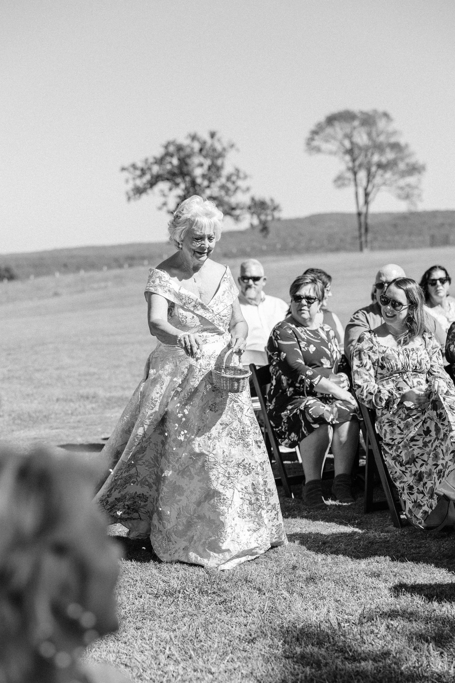 Outdoor wedding ceremony with guests seated on lawn under open sky.