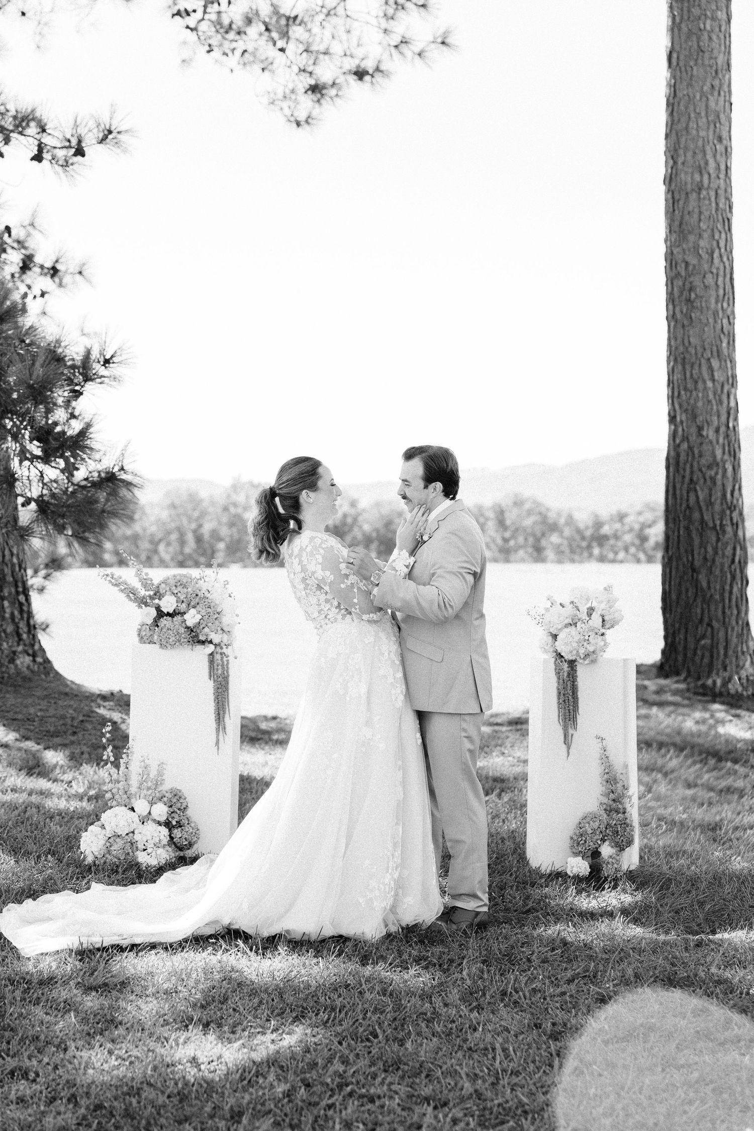 Black and white photo of wedding couple embracing at outdoor ceremony site with floral arrangements.