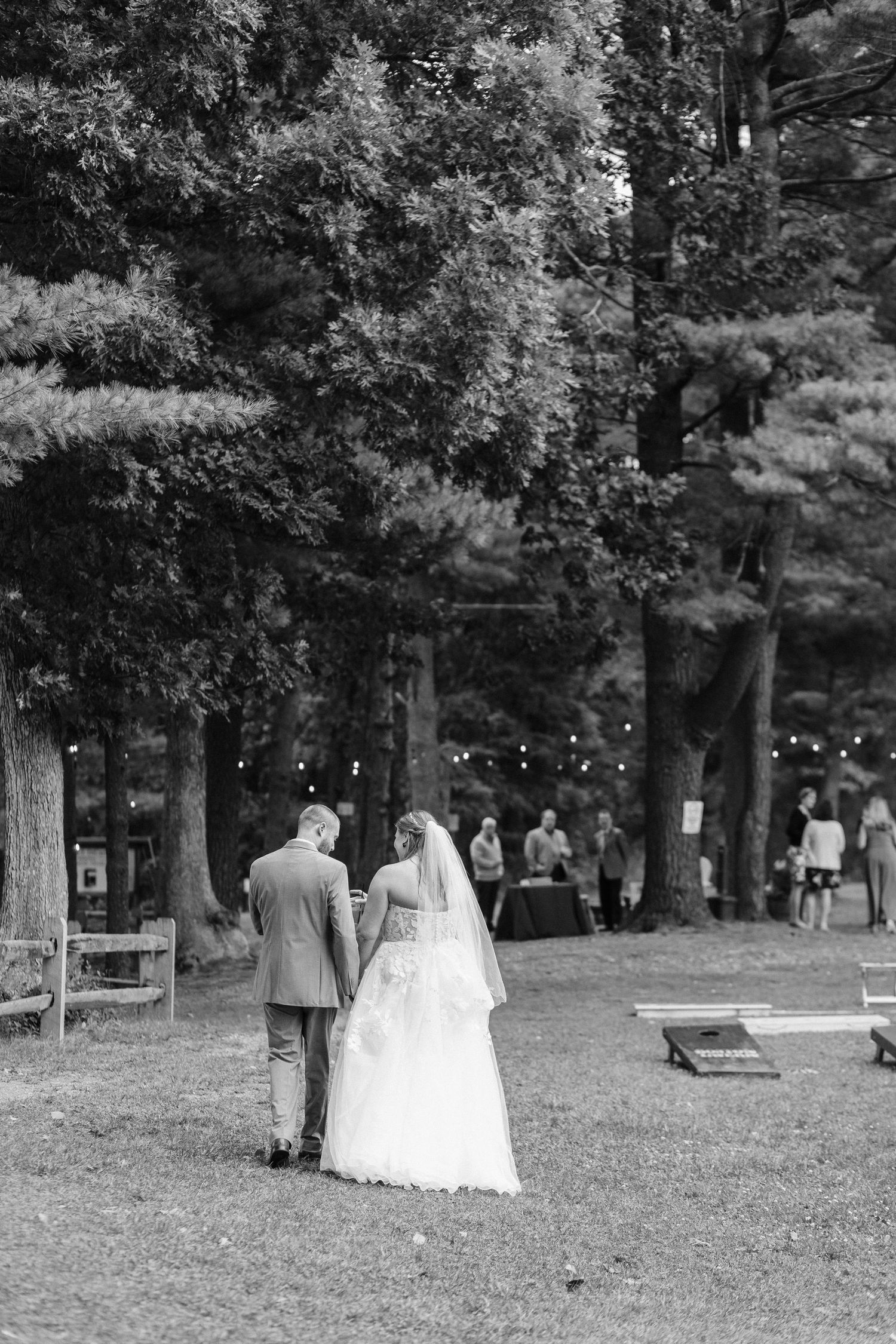 Black and white photo of a couple walking through a tree-lined outdoor venue.
