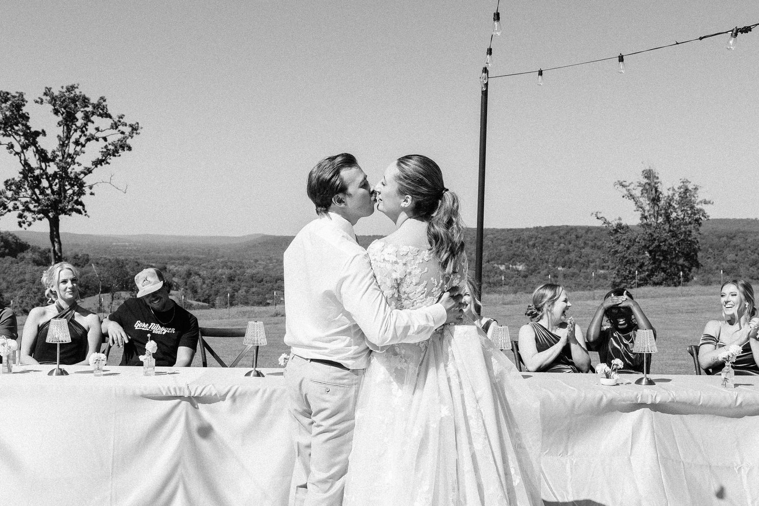Black and white panoramic view of an outdoor wedding reception with string lights.