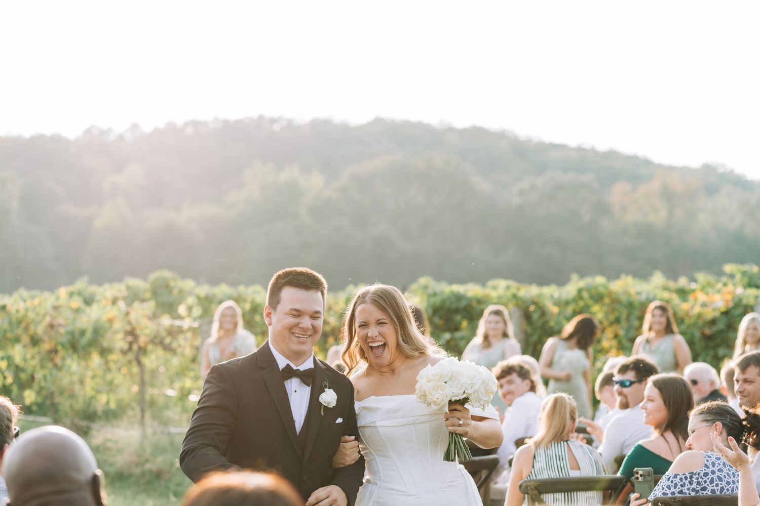 Wedding party celebrates outdoors at sunset with guests mingling and dancing in a scenic mountain setting.
