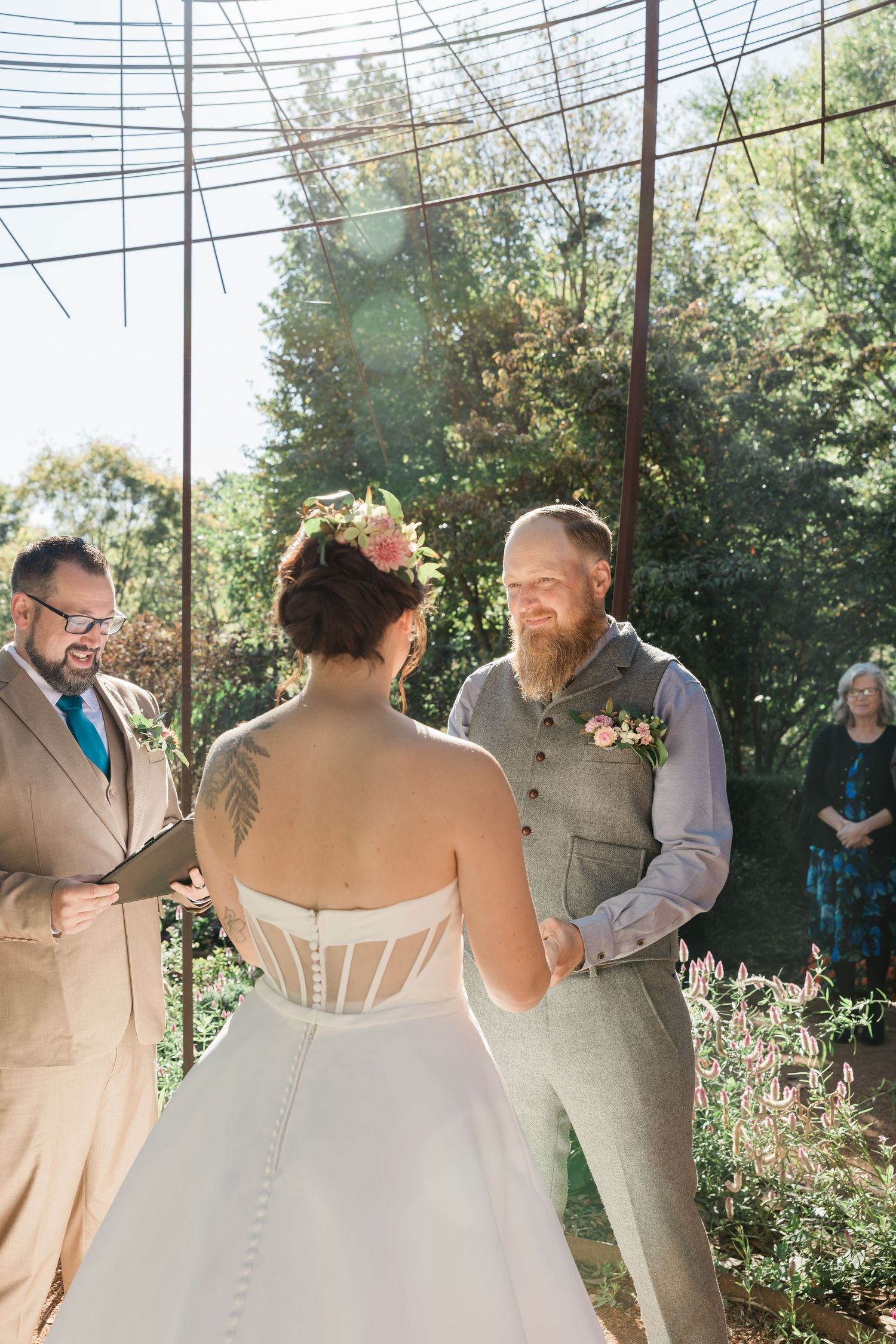 Outdoor wedding ceremony scene with guests gathered under power lines and trees in natural daylight.
