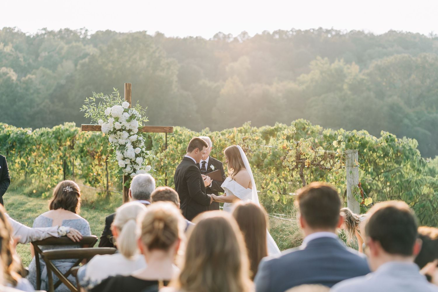 Wedding guests gather outdoors for a scenic ceremony overlooking a beautiful mountain landscape at sunset.