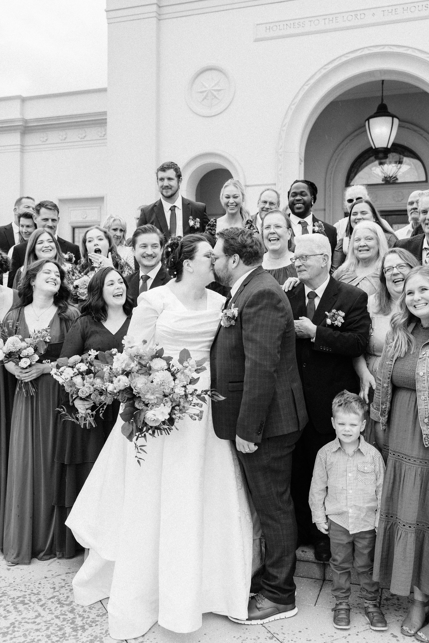Wedding party gathered outside a white church building for a group photo.