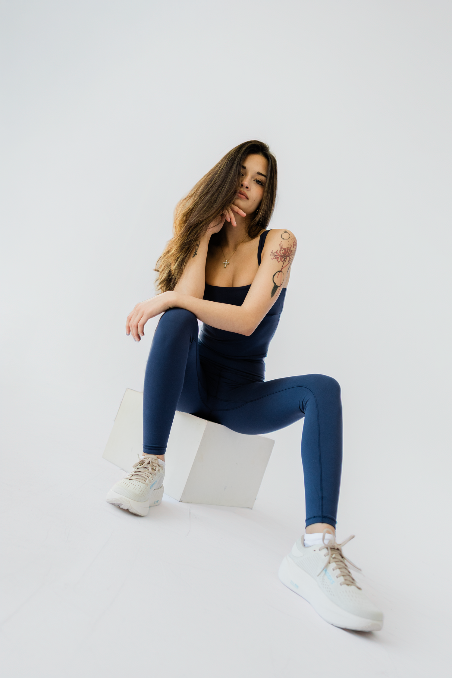 Fashion model in navy blue athletic wear and white sneakers poses against white background in dynamic series.