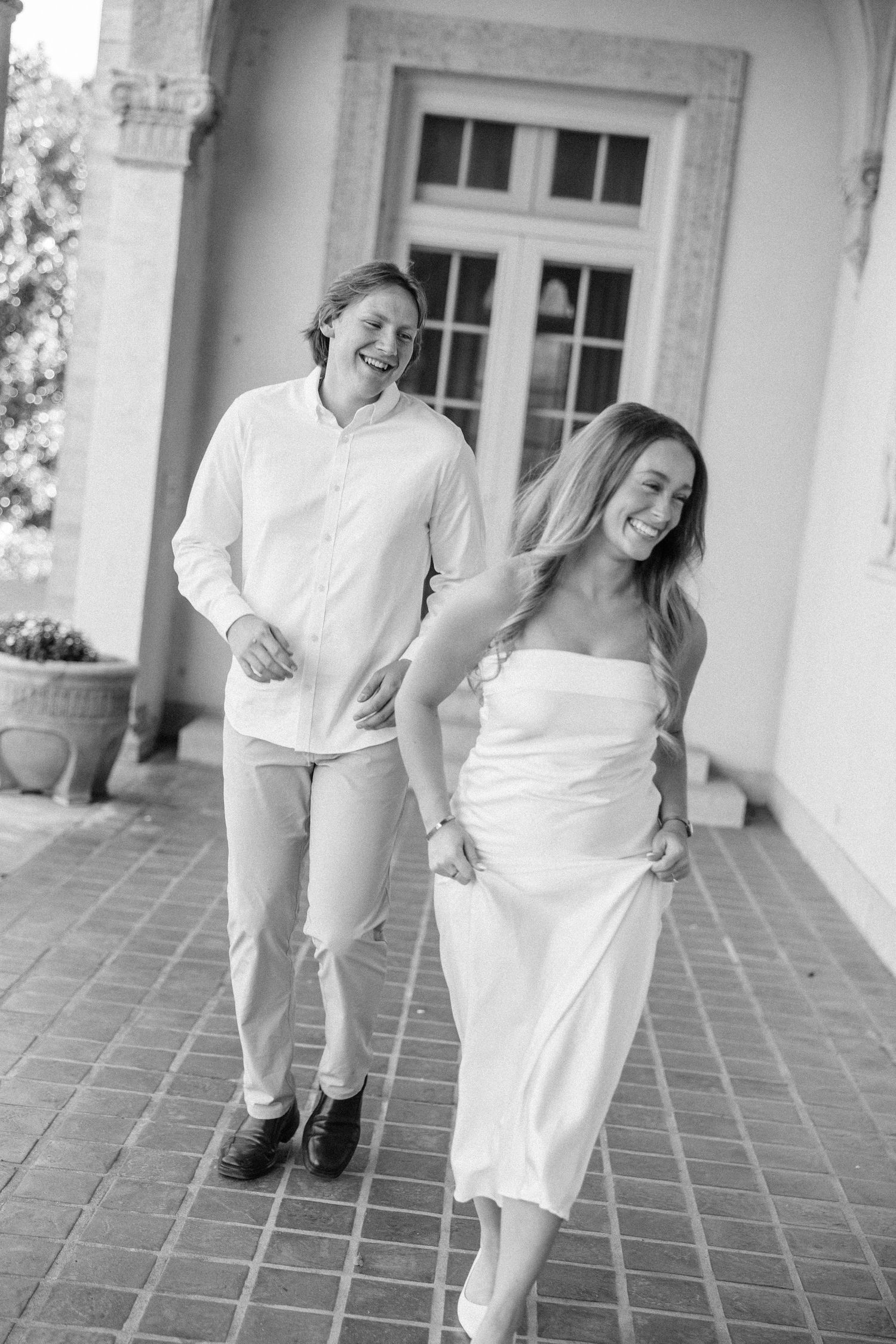 Black and white sequence of three photos showing a couple in white attire dancing playfully on a tiled porch.