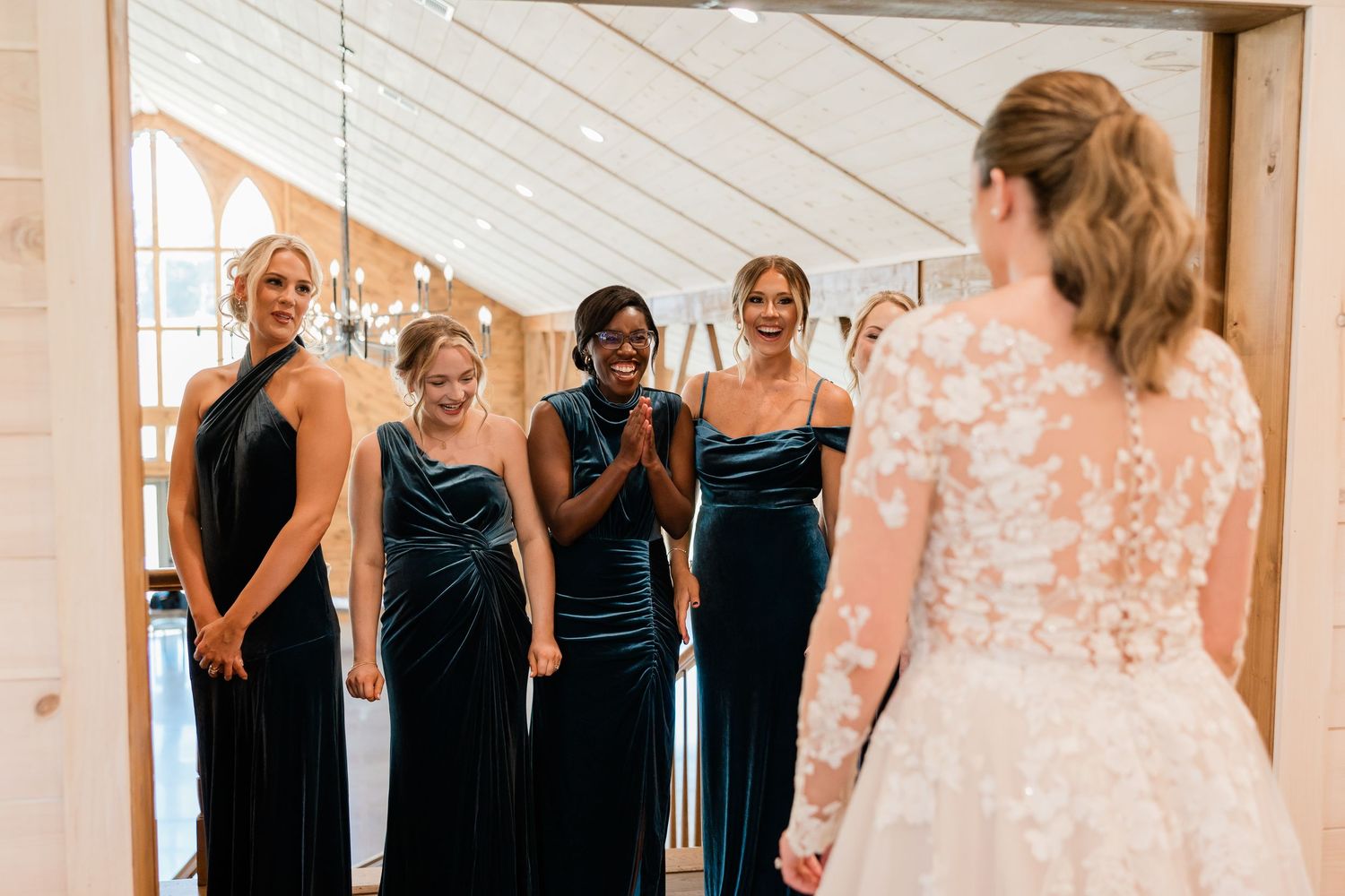 Bridesmaids in navy blue dresses react with joy and excitement during a wedding day first look moment.