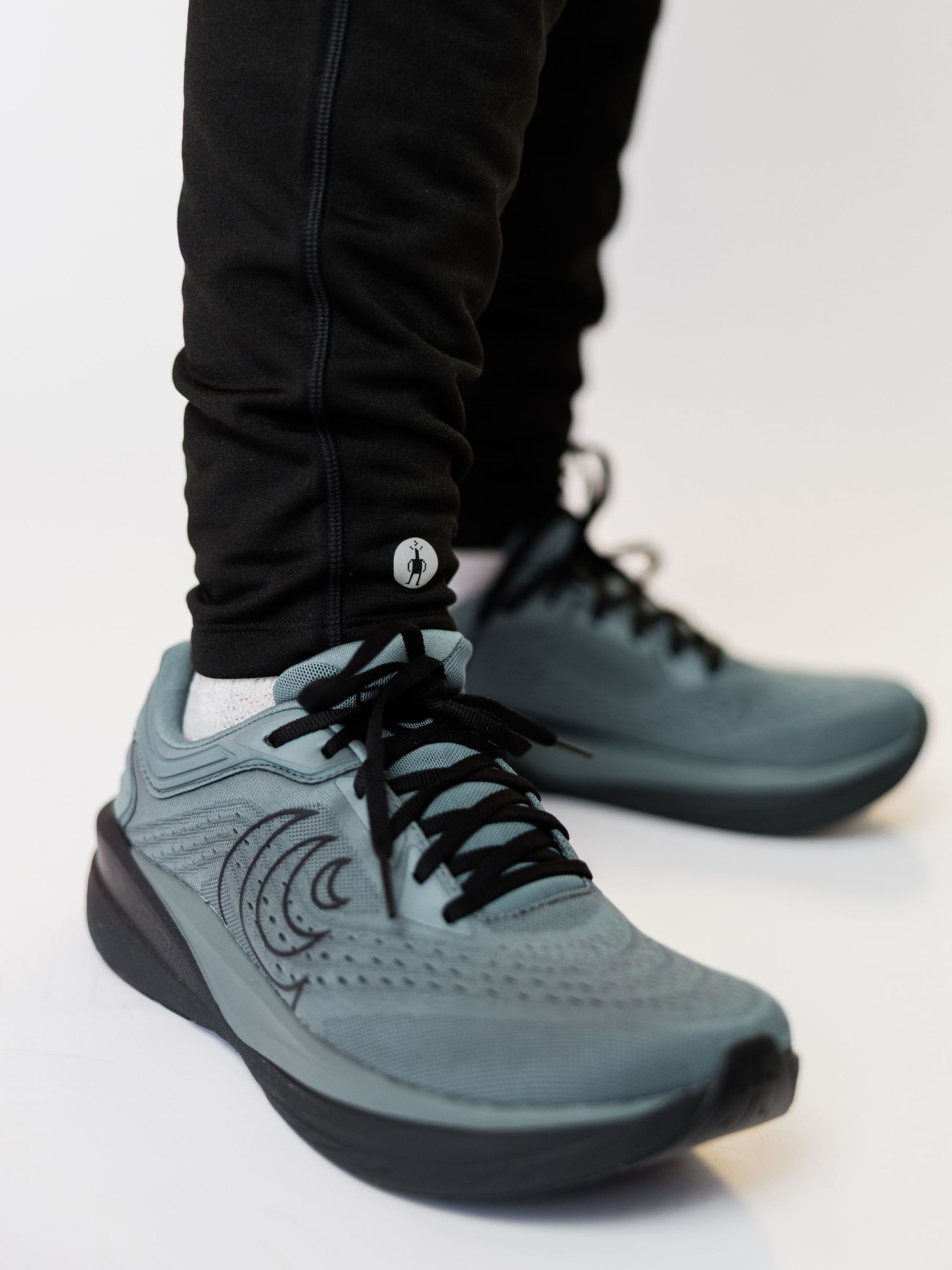 Teal lace-up running sneakers with black sole worn with black jogger pants on white background.