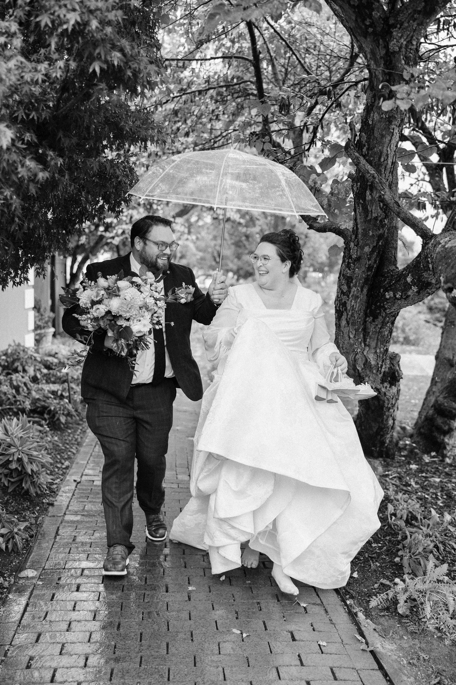 Wedding party walking along brick pathway under tree canopy.