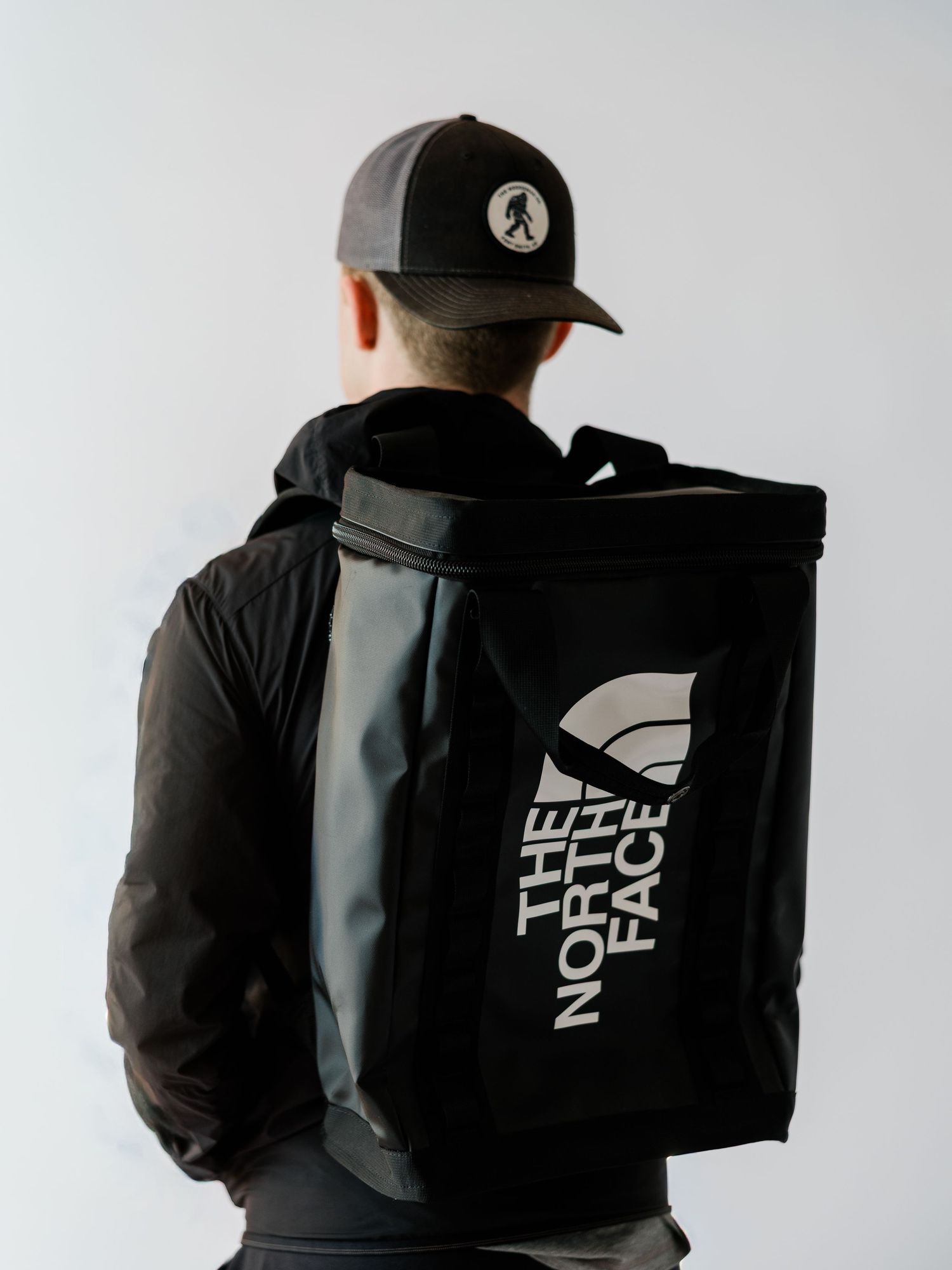 Four views of a black backpack with white text logo shown from different angles against a light background.