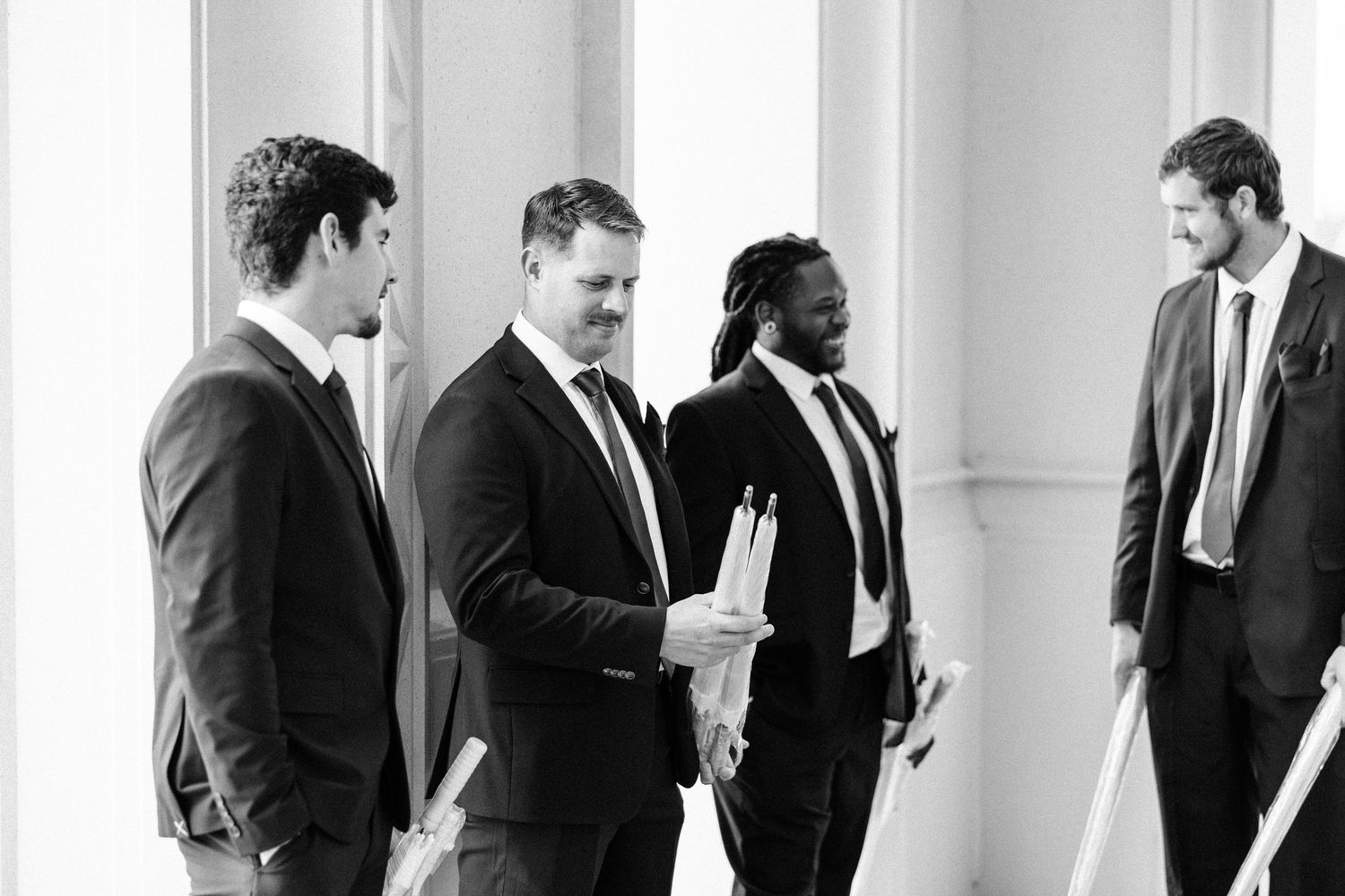 A black and white photo shows a row of businesspeople in suits having conversations in a hallway.