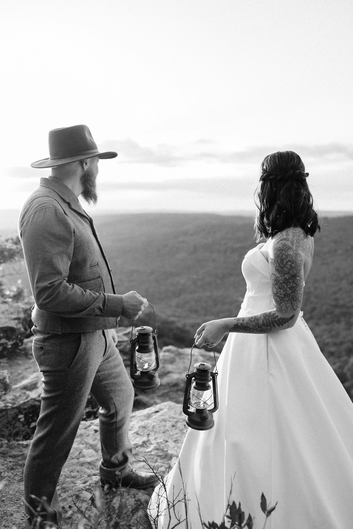 Black and white series of romantic couple with vintage lantern exploring mountainous landscape at sunset.