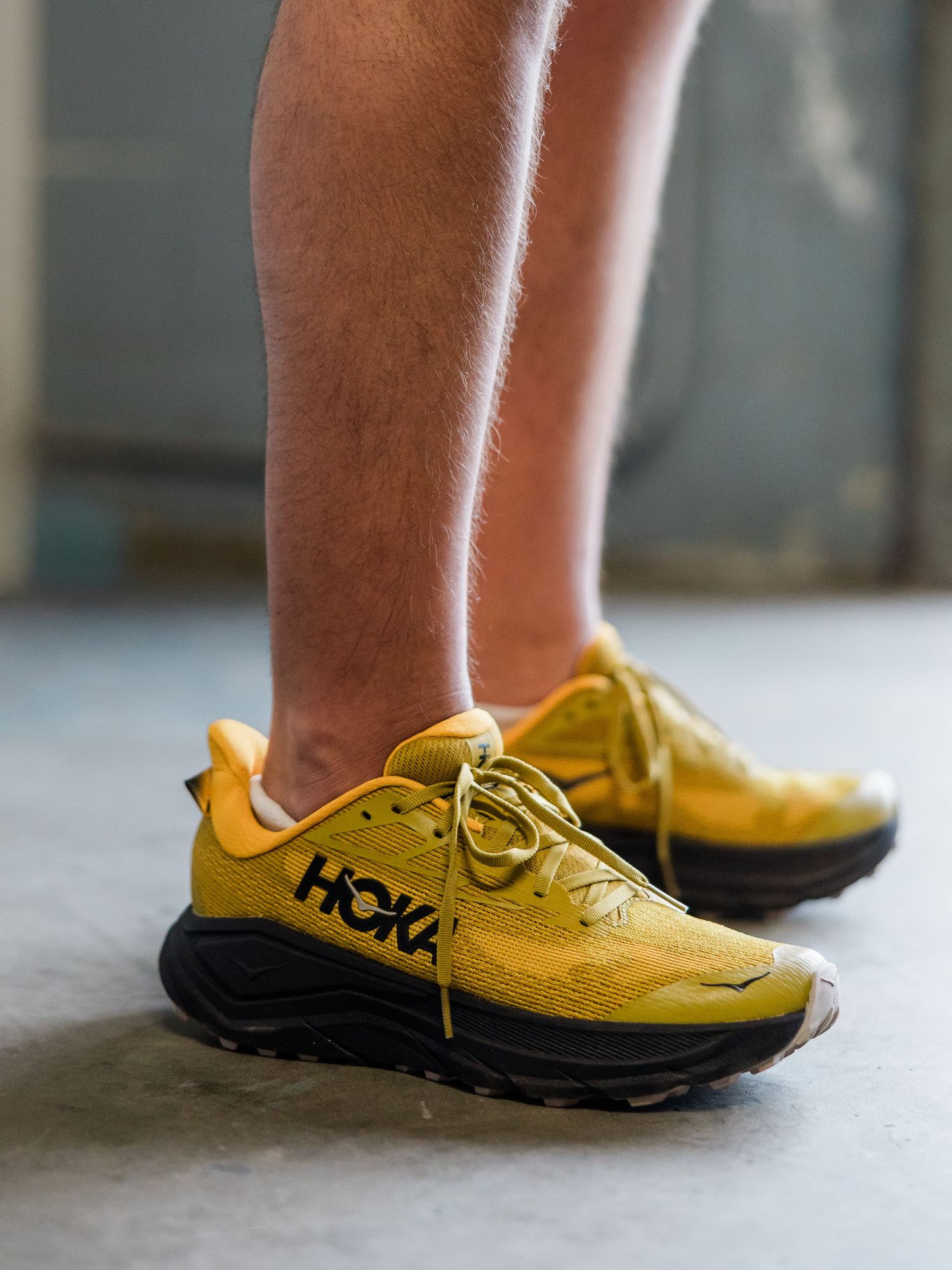 Person wearing bold yellow and black HOKA trail running shoes, showcasing chunky sole design on a neutral background.