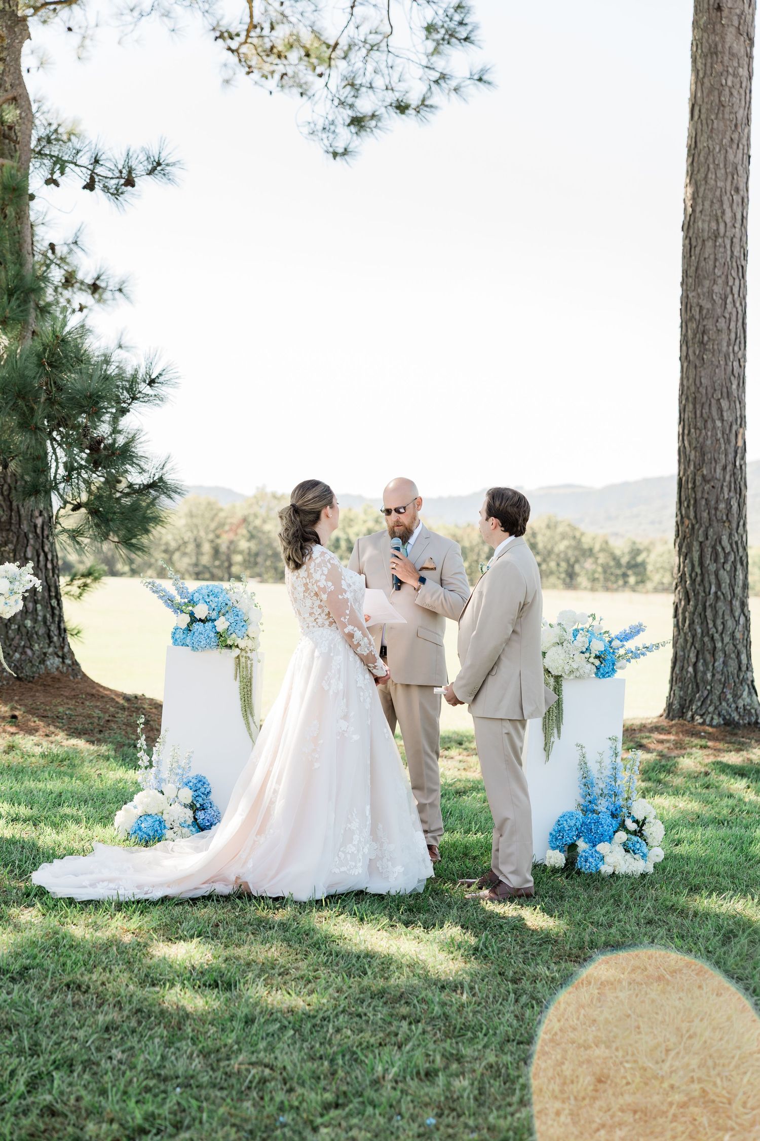 Outdoor wedding scene with blue floral decorations and pine trees in the background.