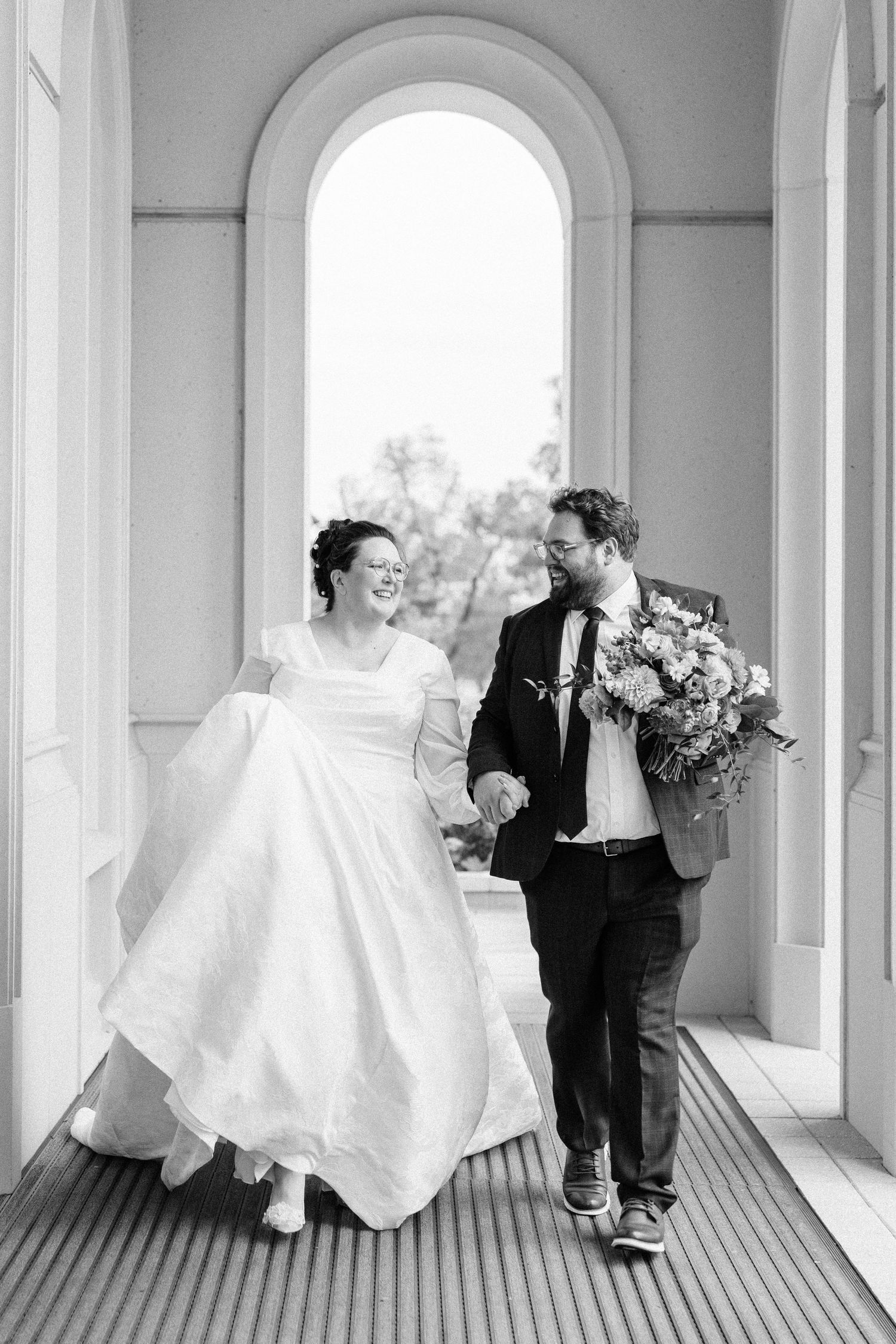 Black and white wedding portraits captured in an elegant colonnade with arched windows.
