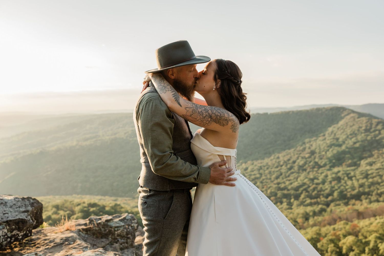 Newlyweds share an intimate moment on a mountain overlook during sunset.