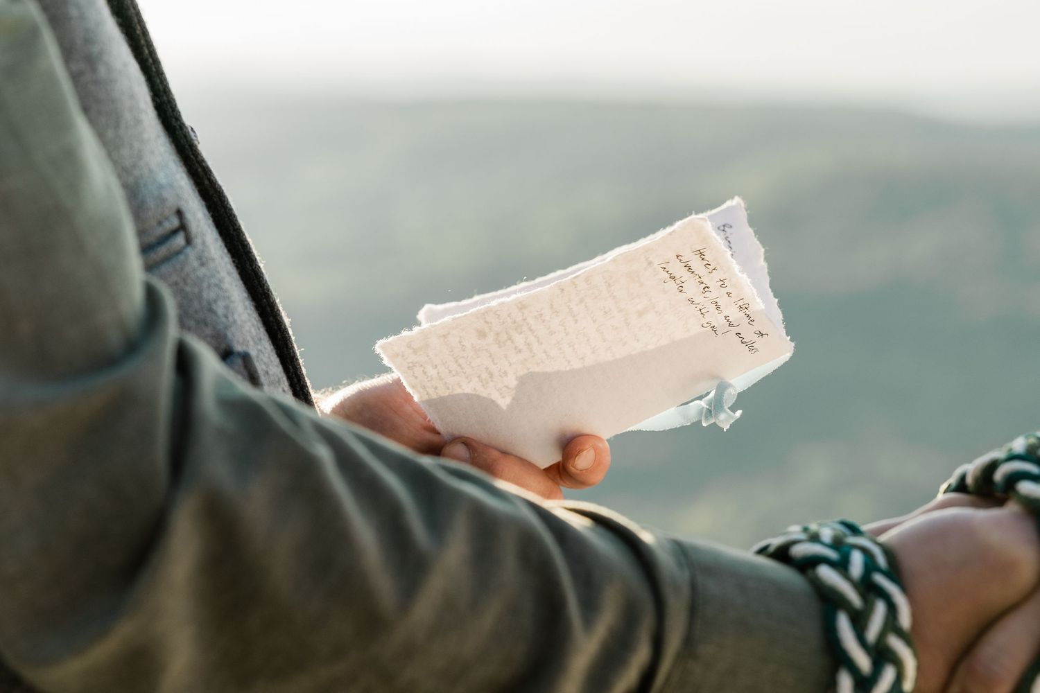 Close up of hands holding handwritten wedding vows against a blurred mountain landscape.
