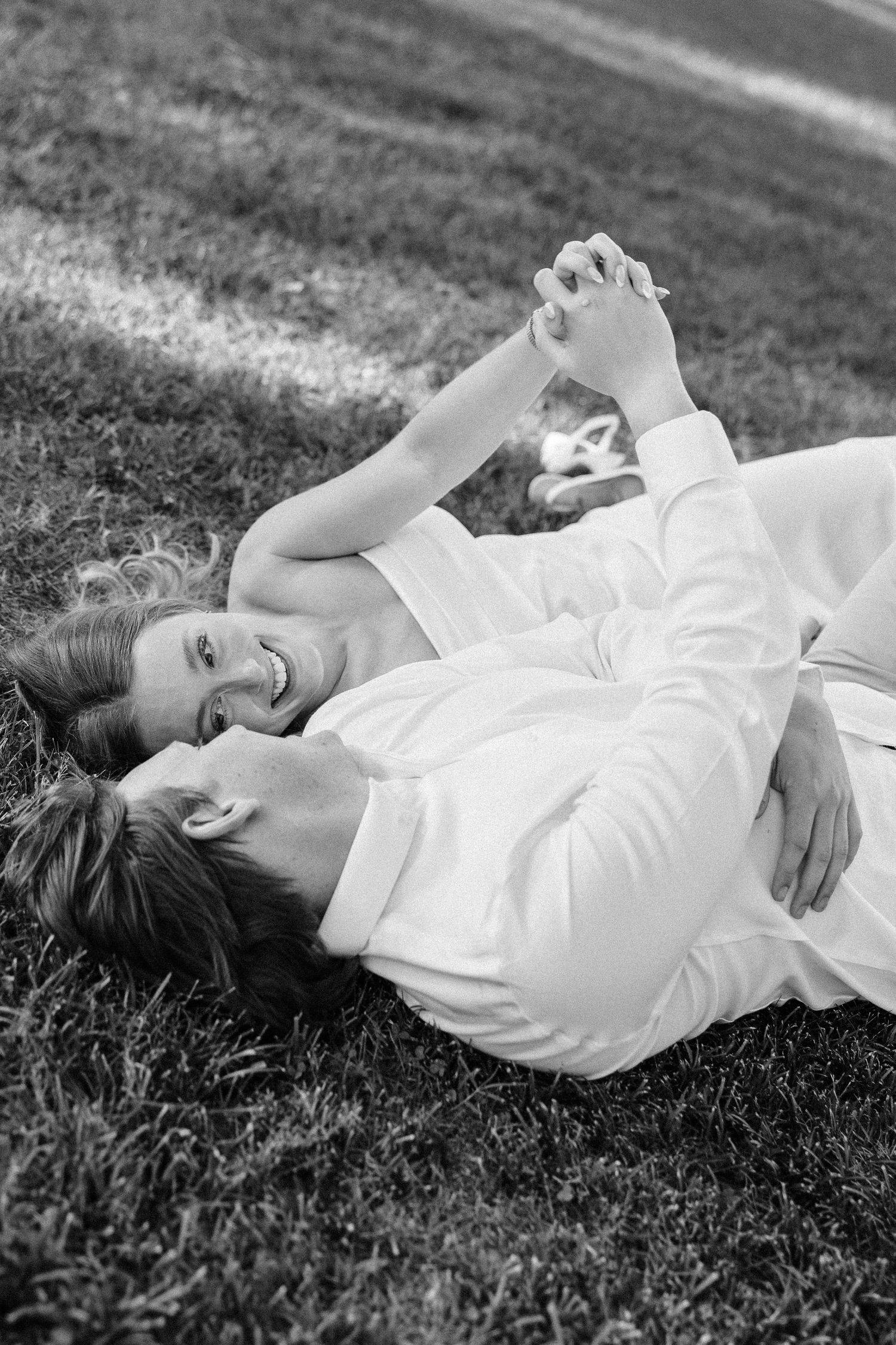 A couple in white clothing lying together on grass in black and white photography.