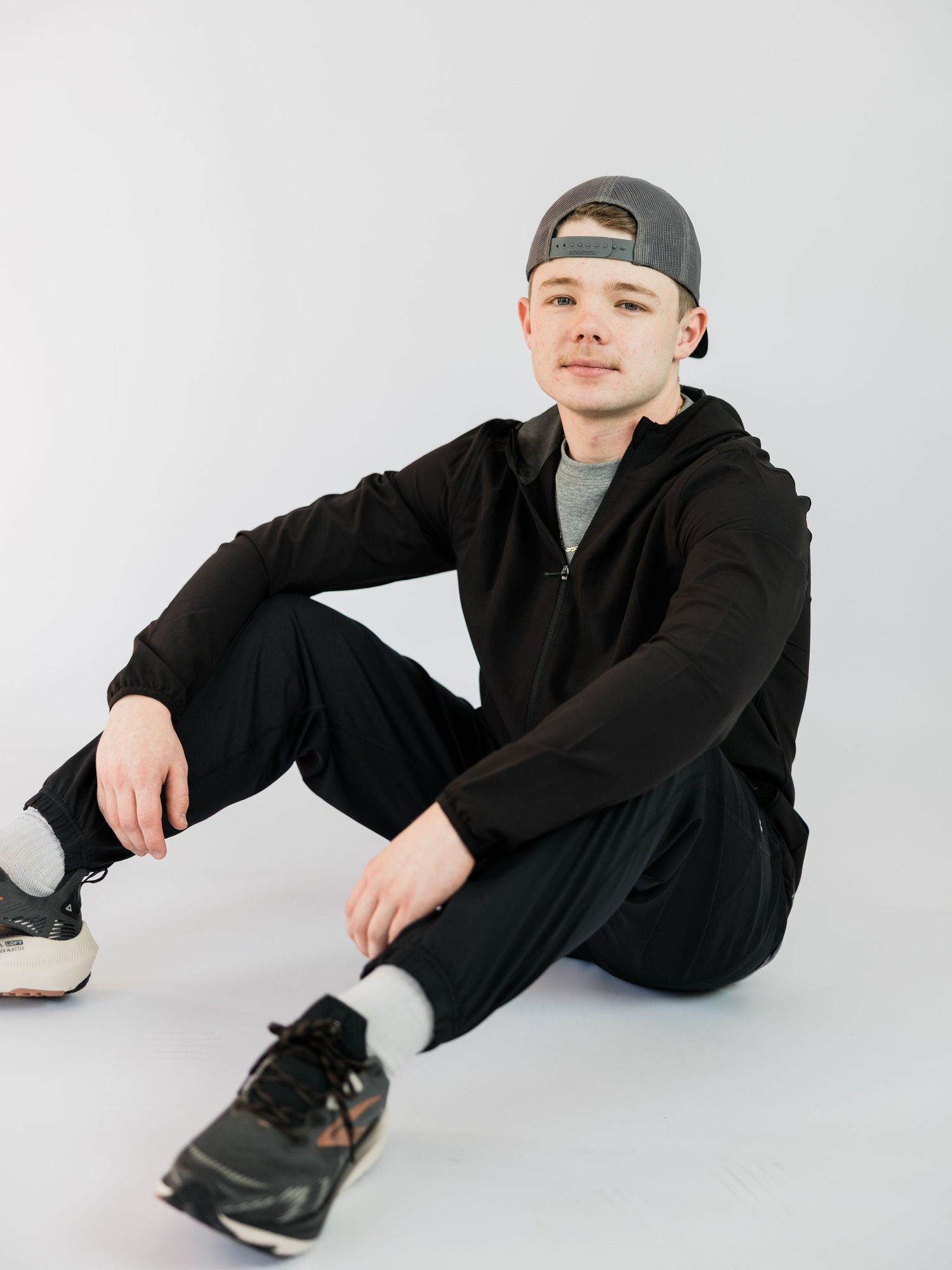 A person in black clothing lying on a white background in four different relaxed poses.