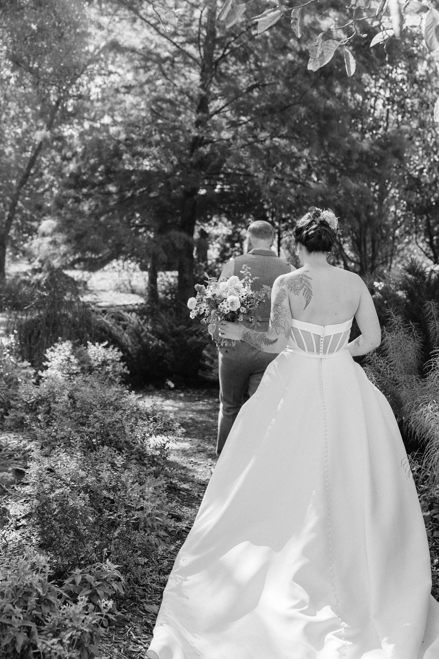 Back view of elegant white wedding dress with flowing train photographed in garden setting.