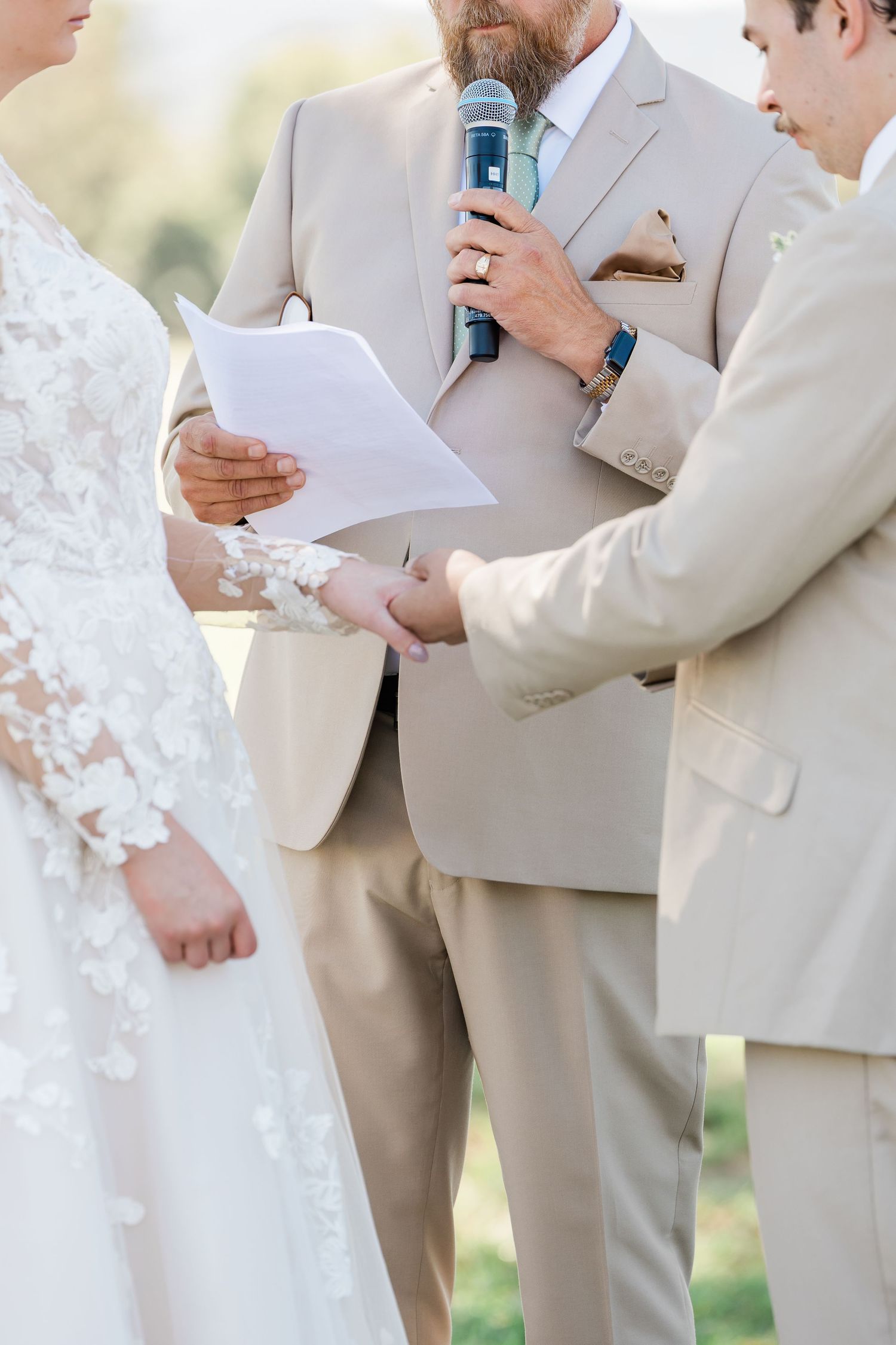 Wedding ceremony participants in light colored attire exchanging vows outdoors.