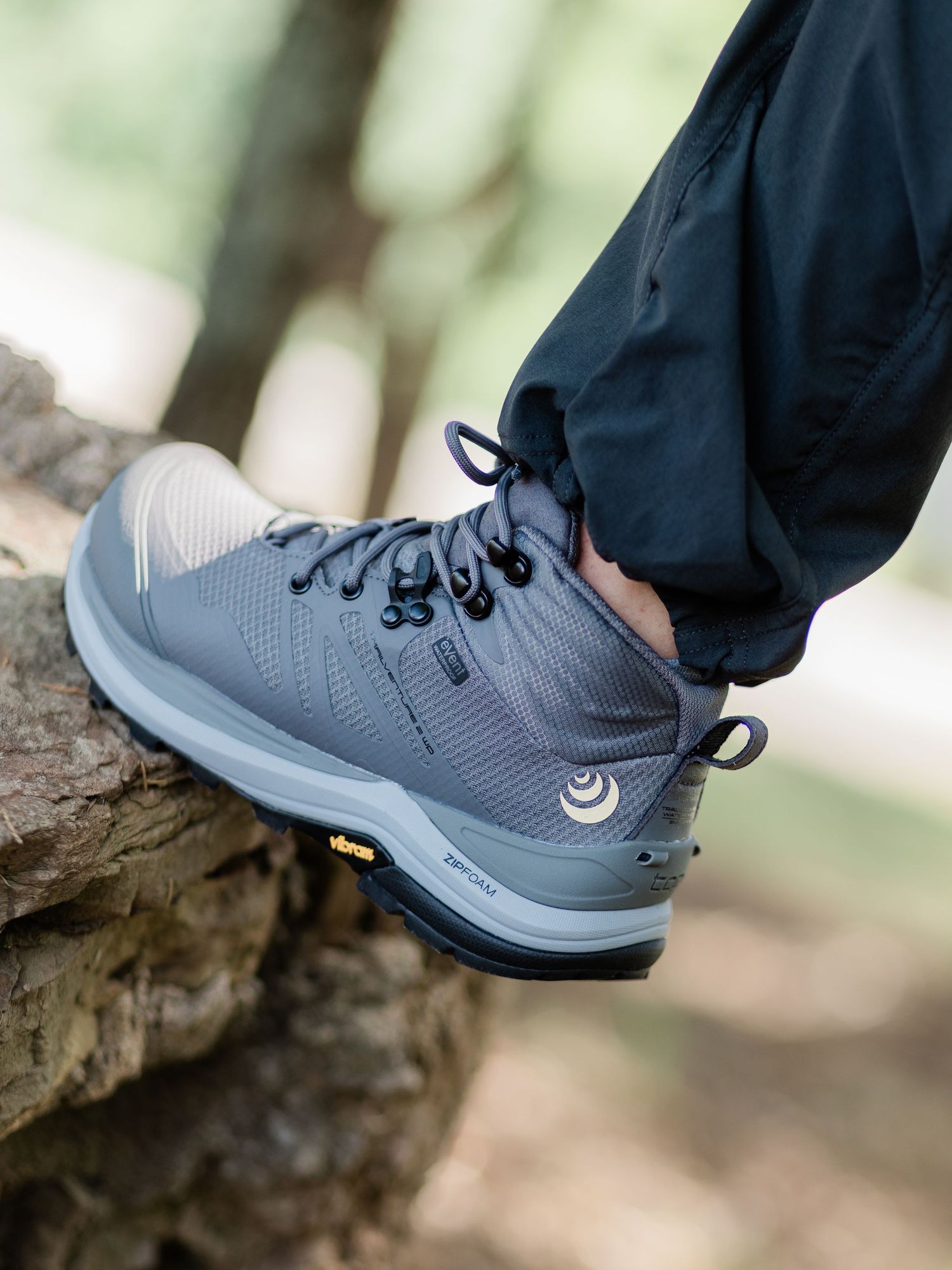 Gray mid-top hiking boot with black laces on a rocky surface, featuring vibram sole and moisture-wicking mesh upper.