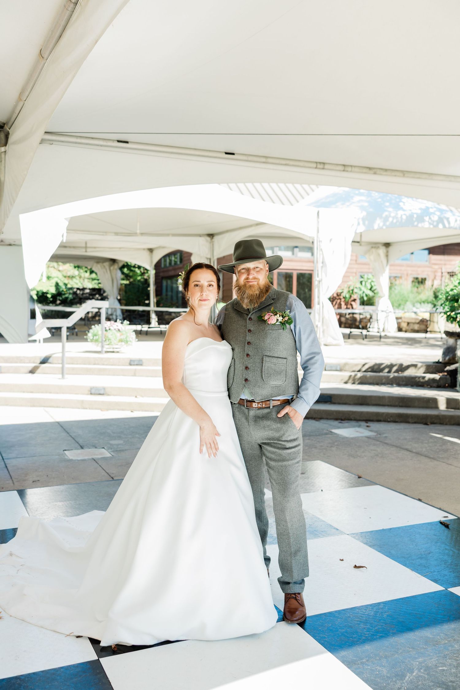A wedding couple sharing a tender moment under a white tent in a parking area.