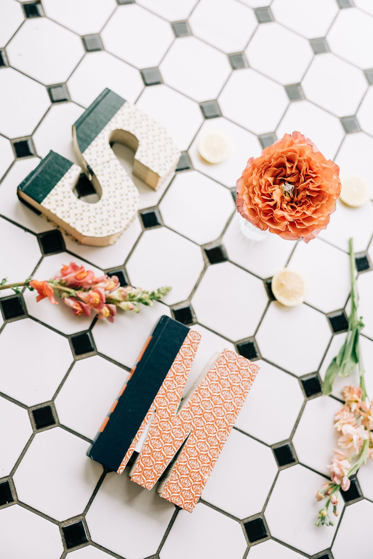 Coral colored paper fans and flowers arranged on white hexagonal tile with black accents create an elegant flat lay composition.