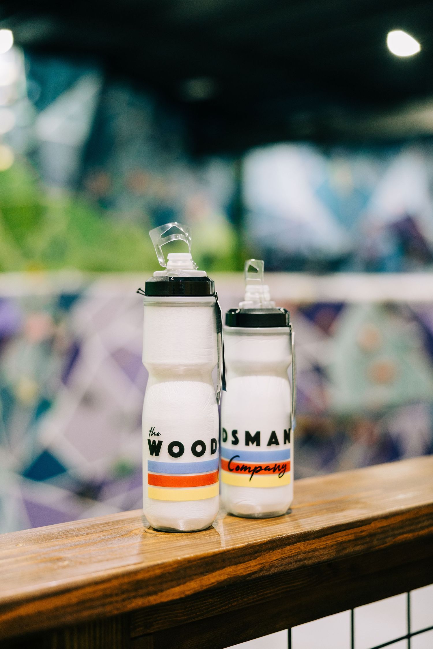 Two white squeeze water bottles branded with The Woodsman Company logo on a wooden shelf.