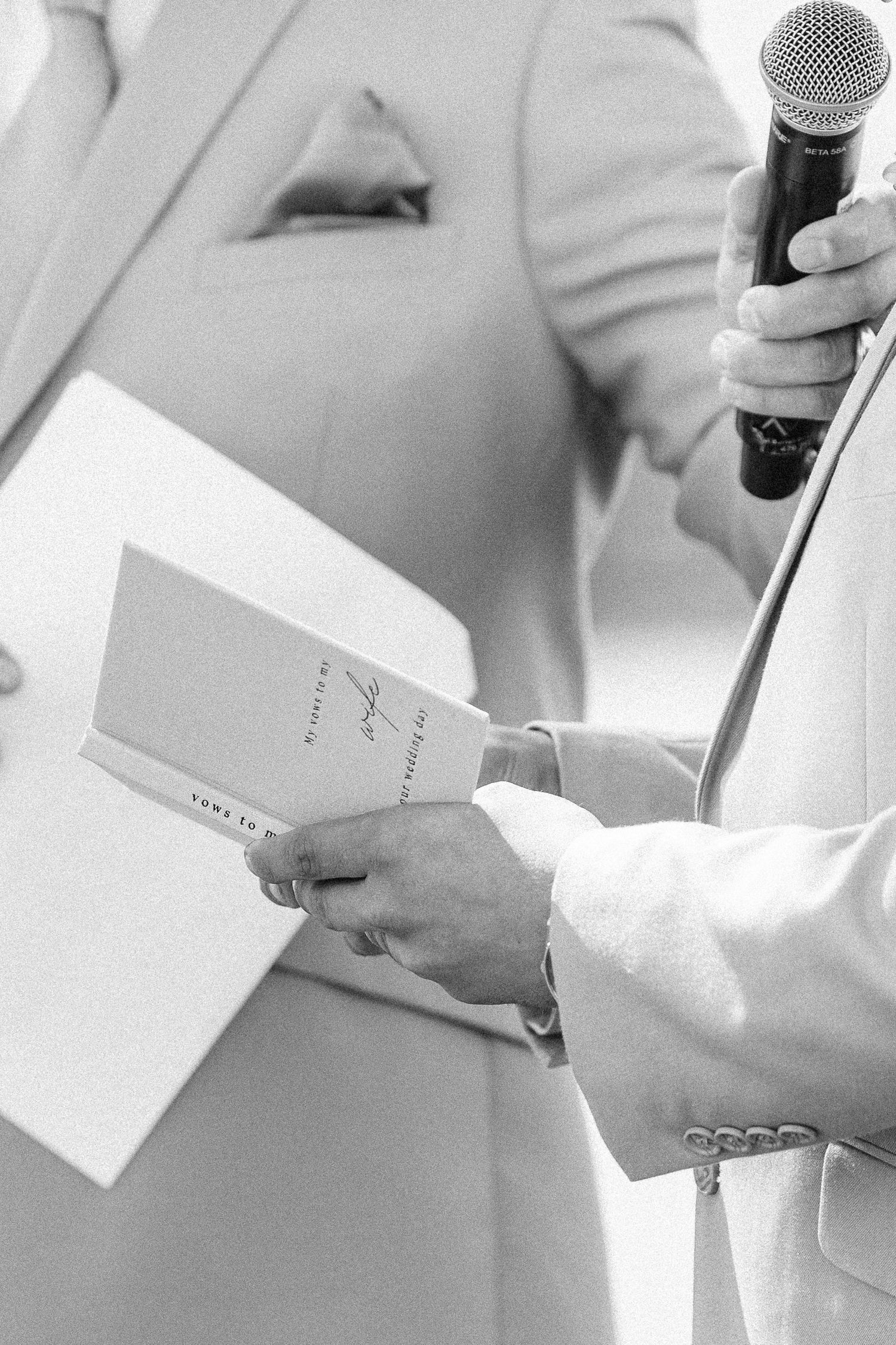 Black and white image of hands holding microphones and papers during a wedding ceremony.
