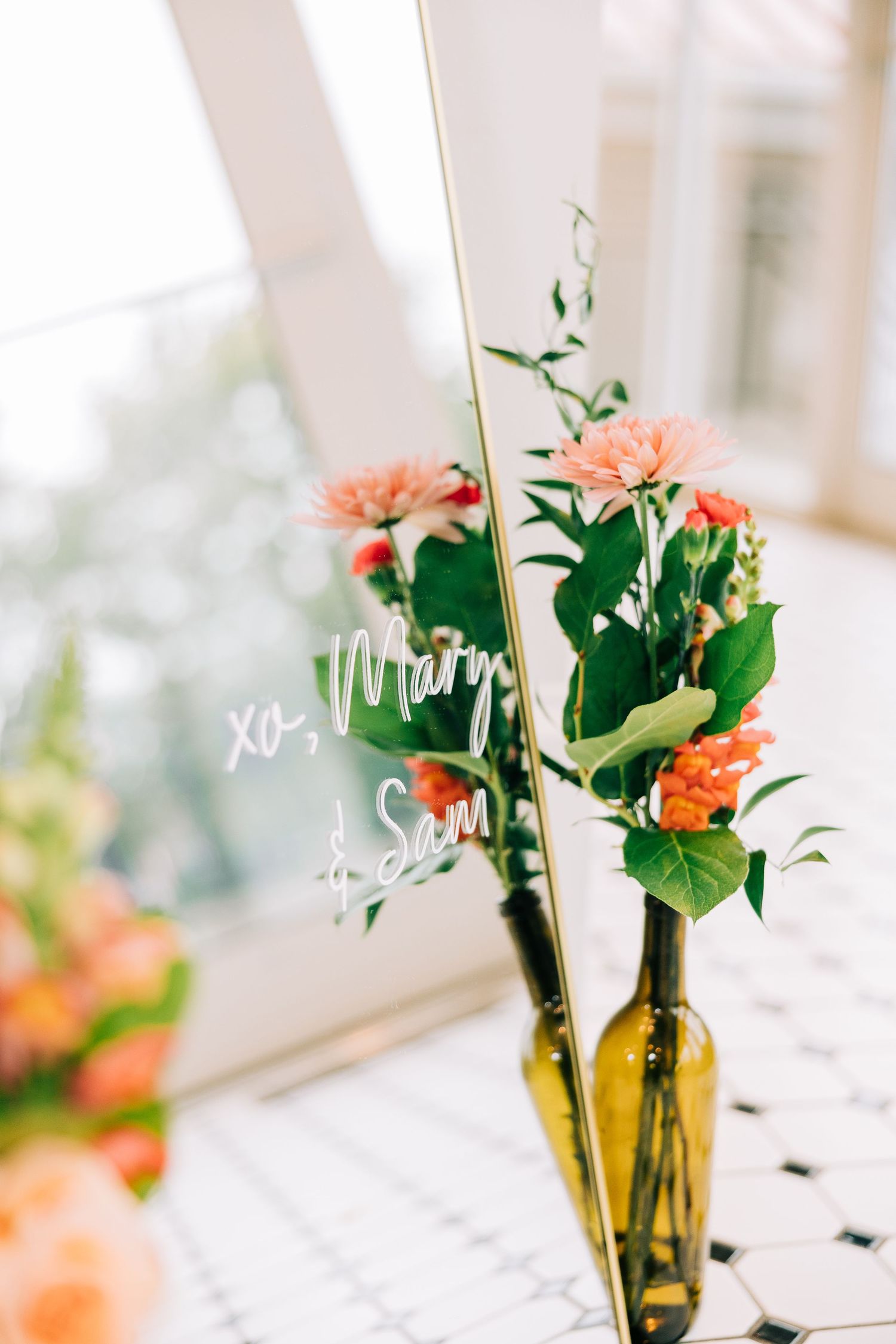 Orange flowers in amber glass vases create an elegant centerpiece display on a white surface in natural lighting.