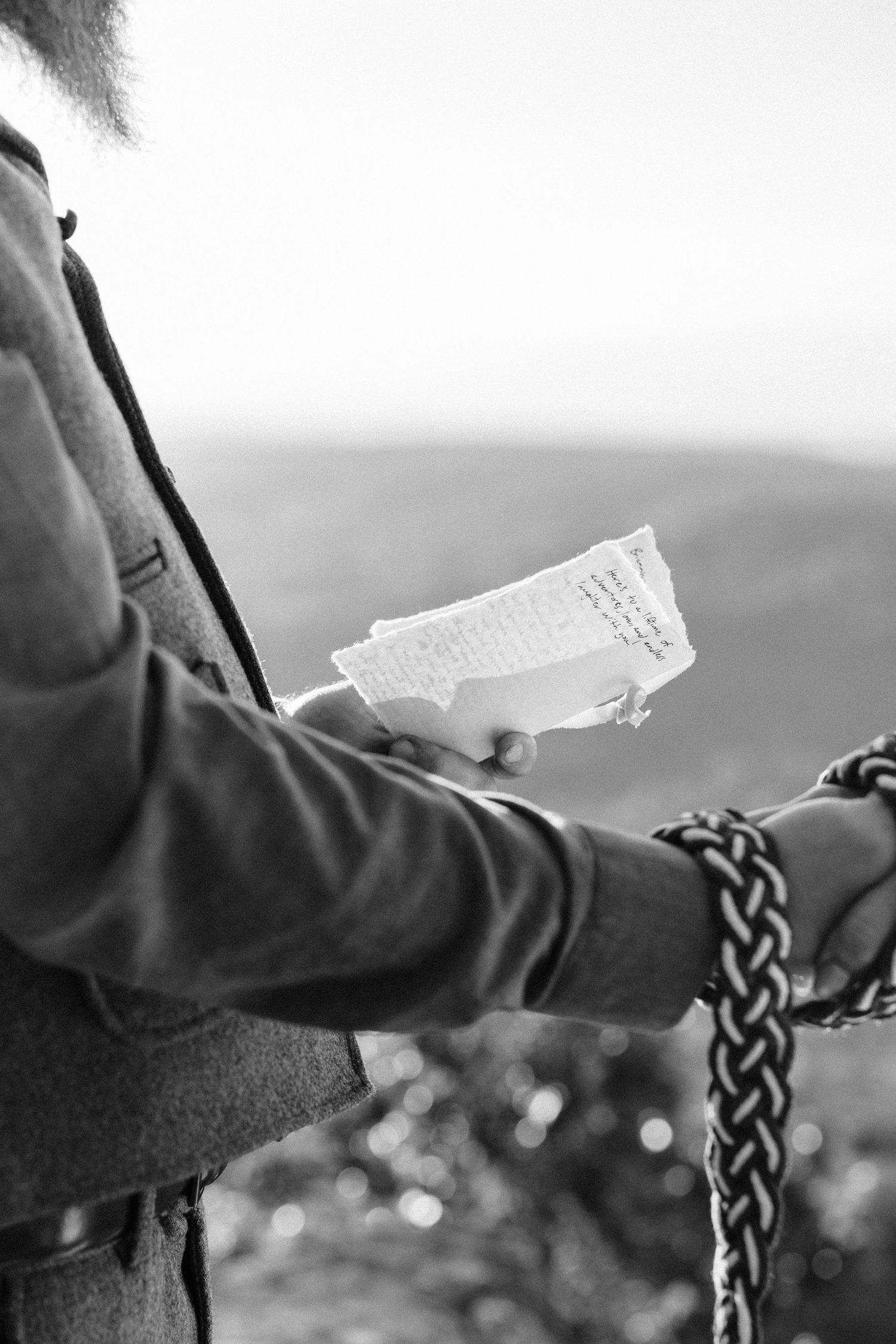 Close-up black and white shot of hands holding a piece of paper against a blurred outdoor background.