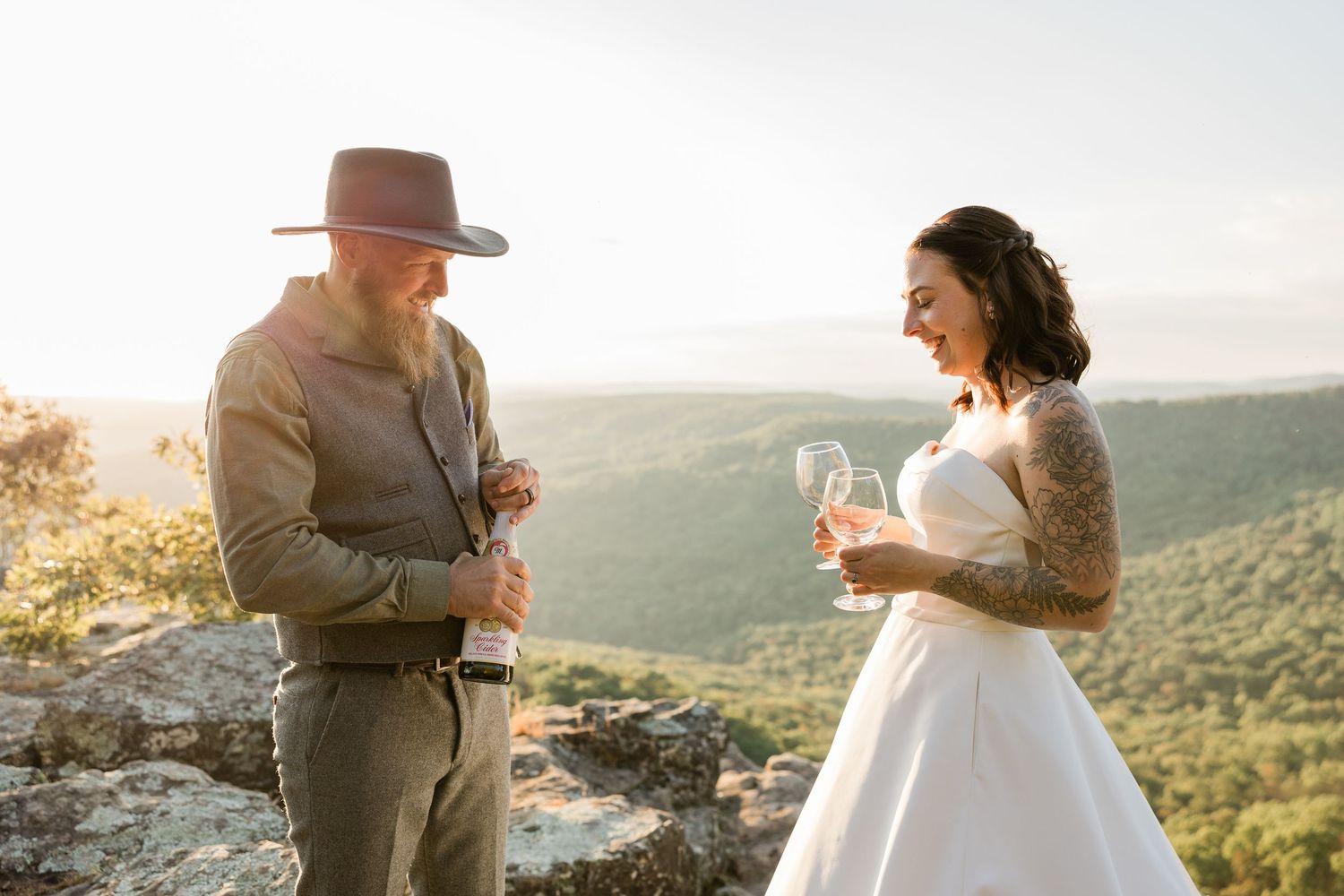A couple shares a toast at sunset on a mountain overlook during their wedding celebration.