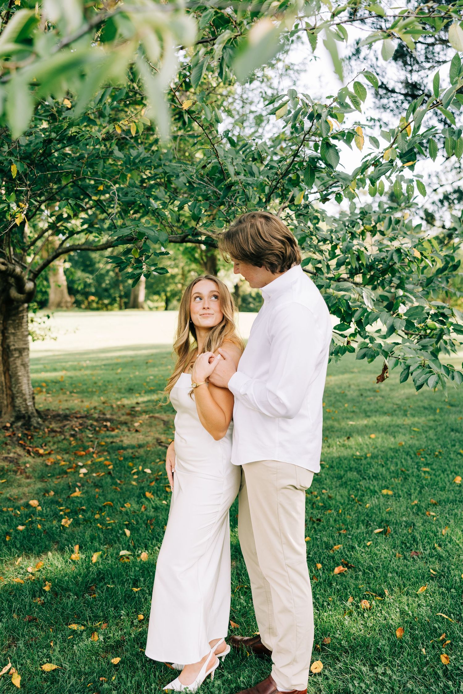 A couple in white clothing shares tender moments together in a sunlit orchard on a summer afternoon.
