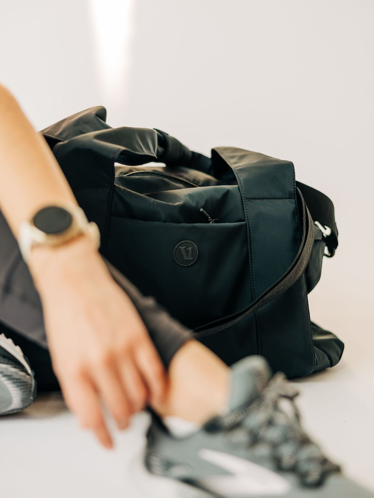 Black Lululemon gym duffel bag next to athletic sneakers, with a person wearing a gold watch reaching into the bag.
