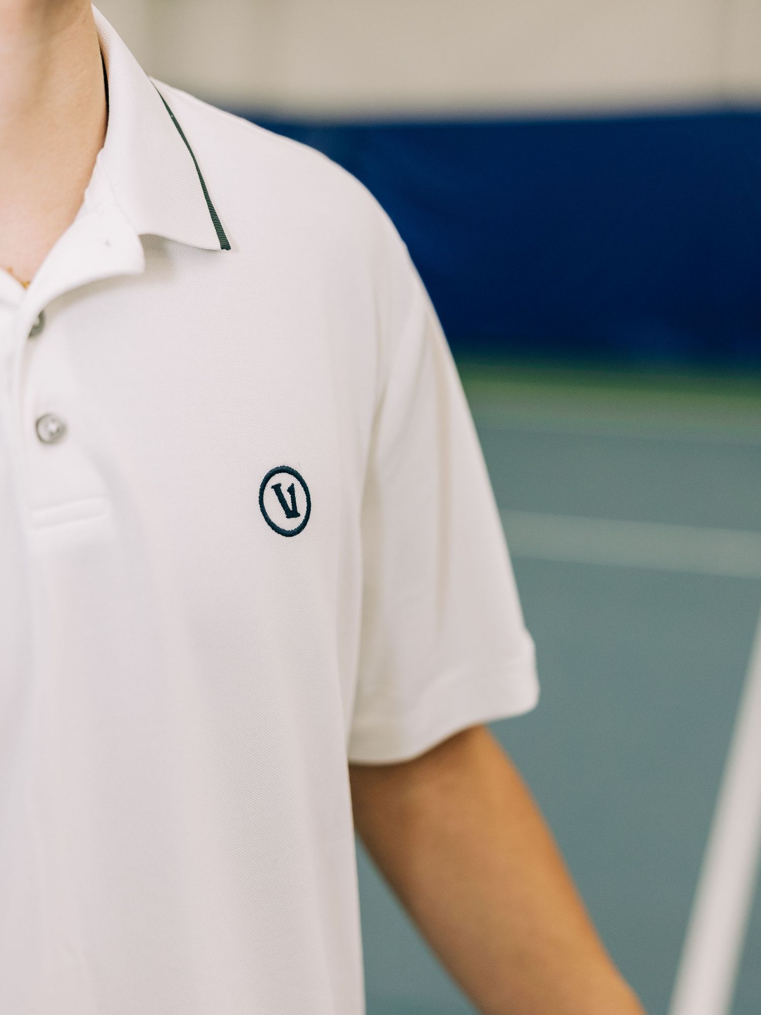 White polo shirt with circular logo detail, worn on a tennis court.