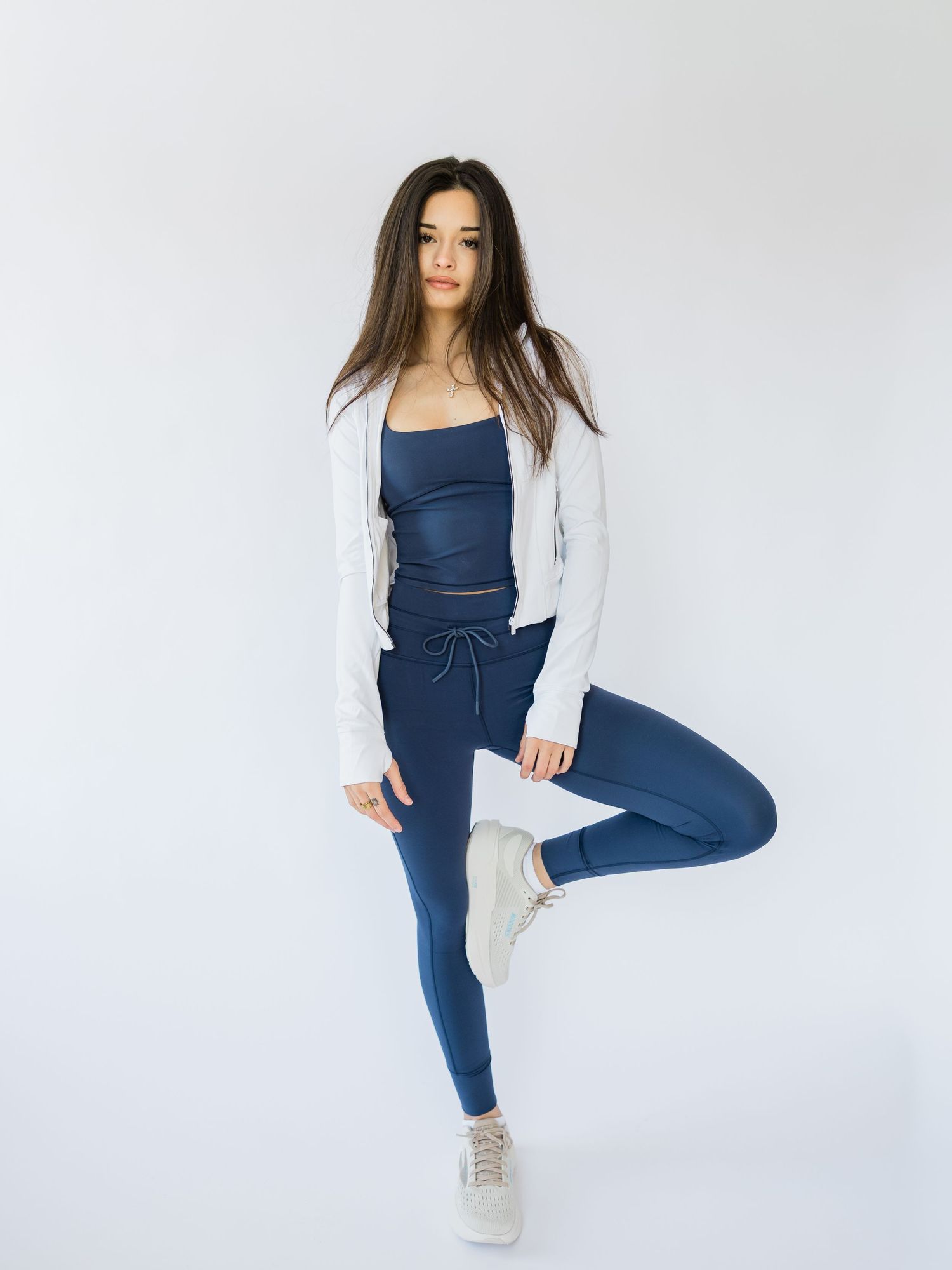 Woman wearing navy blue activewear set with white cardigan poses in different yoga-inspired positions against white background.