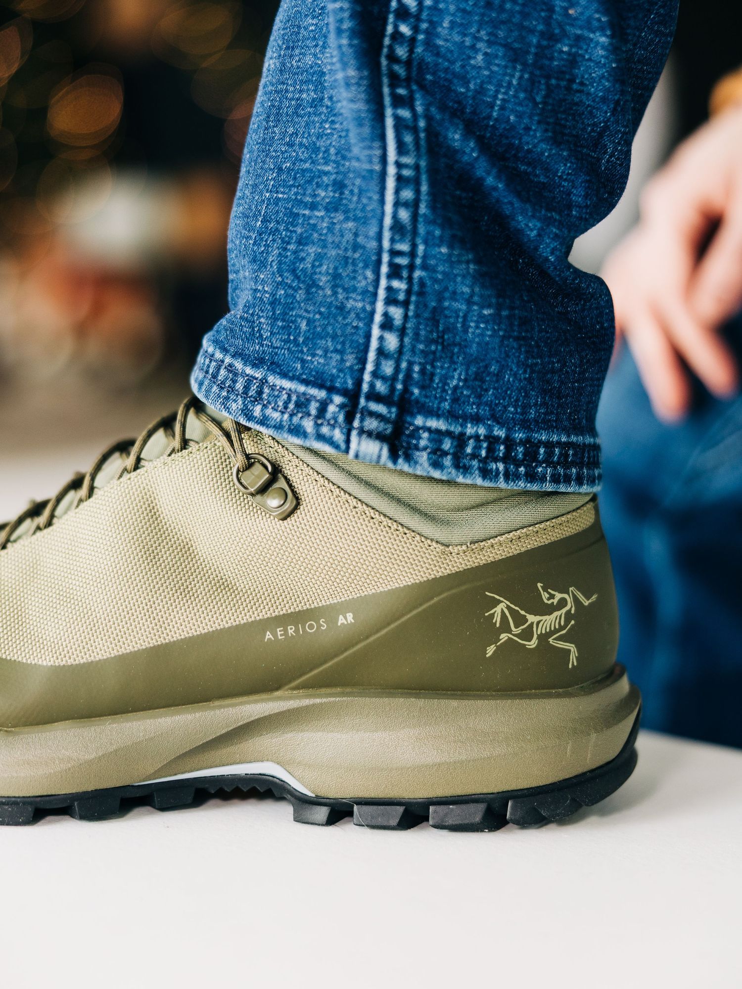 Close-up side view of an olive green hiking shoe with beige laces against a blurred background.