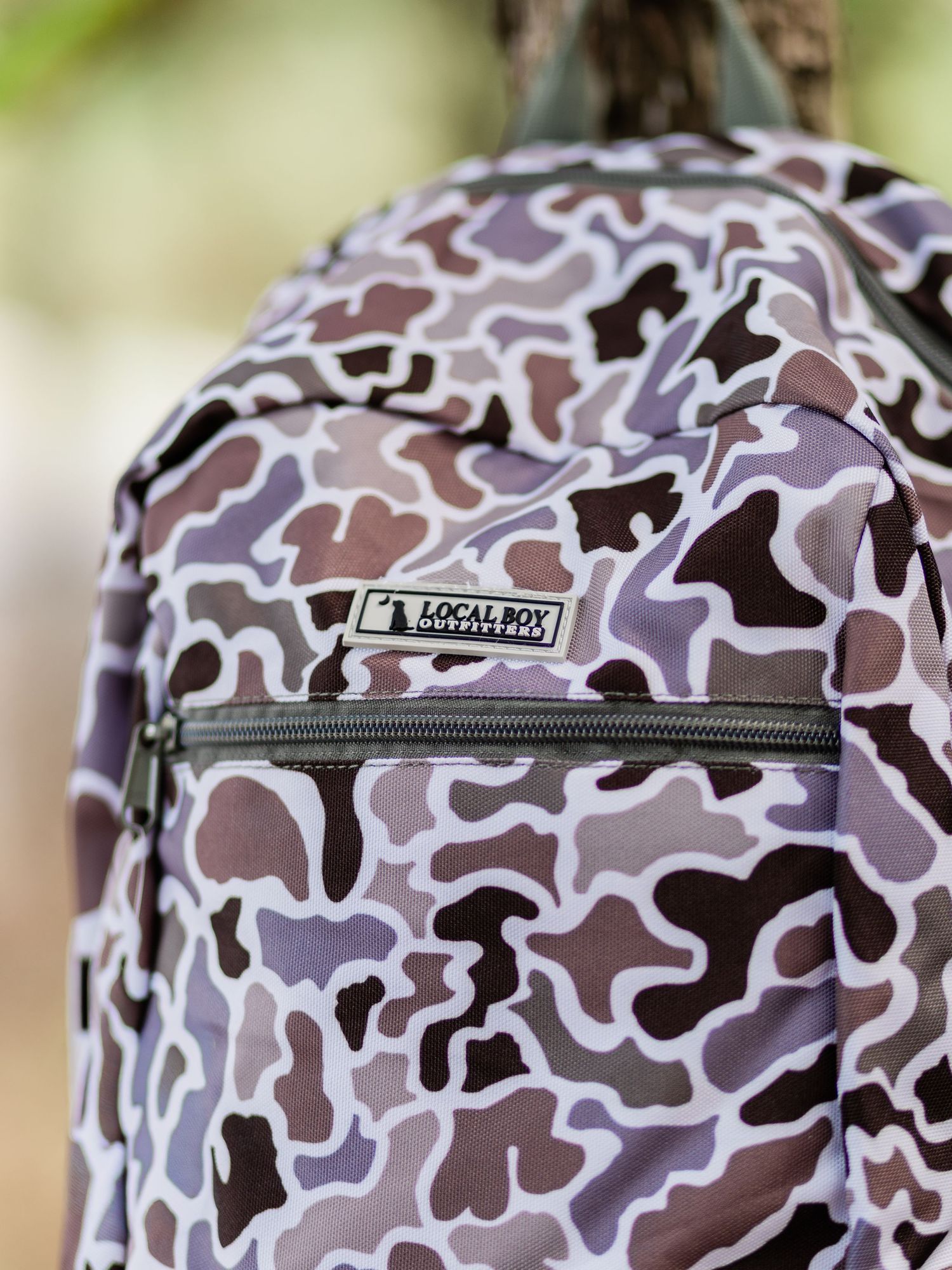 Local Boy Outfitters camo backpack in purple and brown tones, featuring a zippered front pocket.