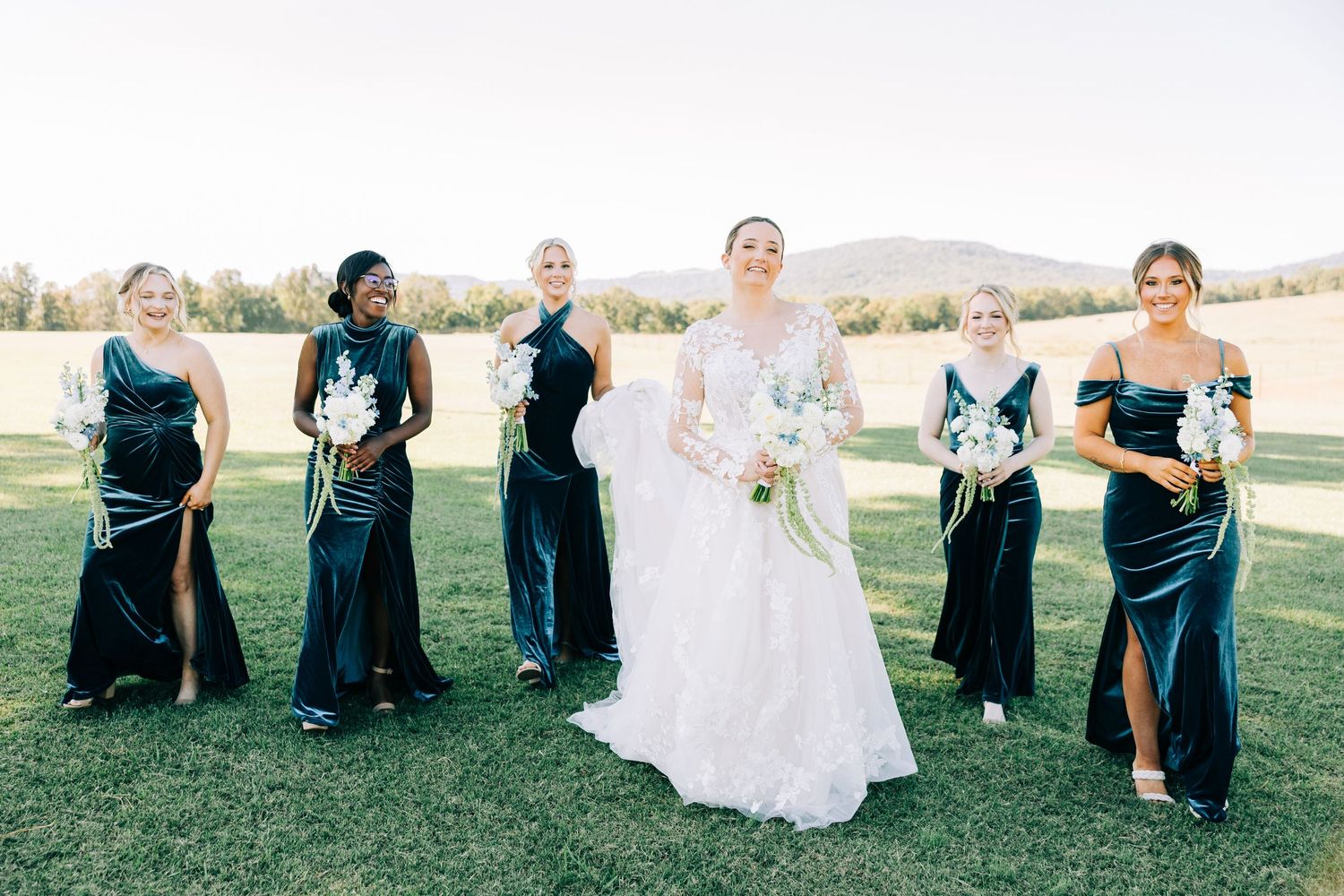 Bridal party in navy dresses laughing together on a sunny outdoor lawn.