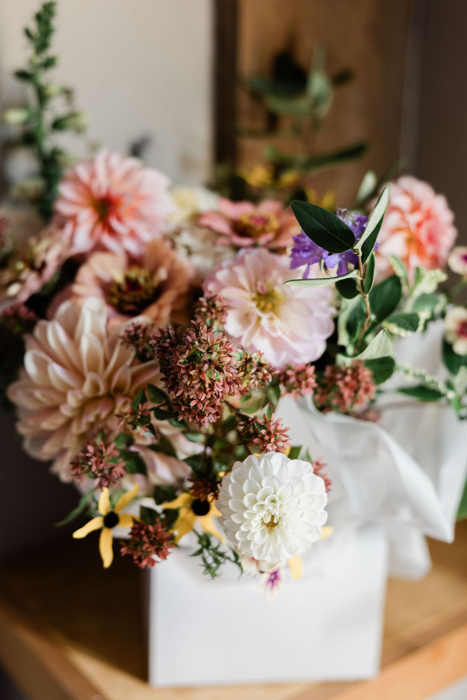 Pink and peach dahlias with greenery arranged in a modern white ceramic vase create an elegant floral centerpiece.