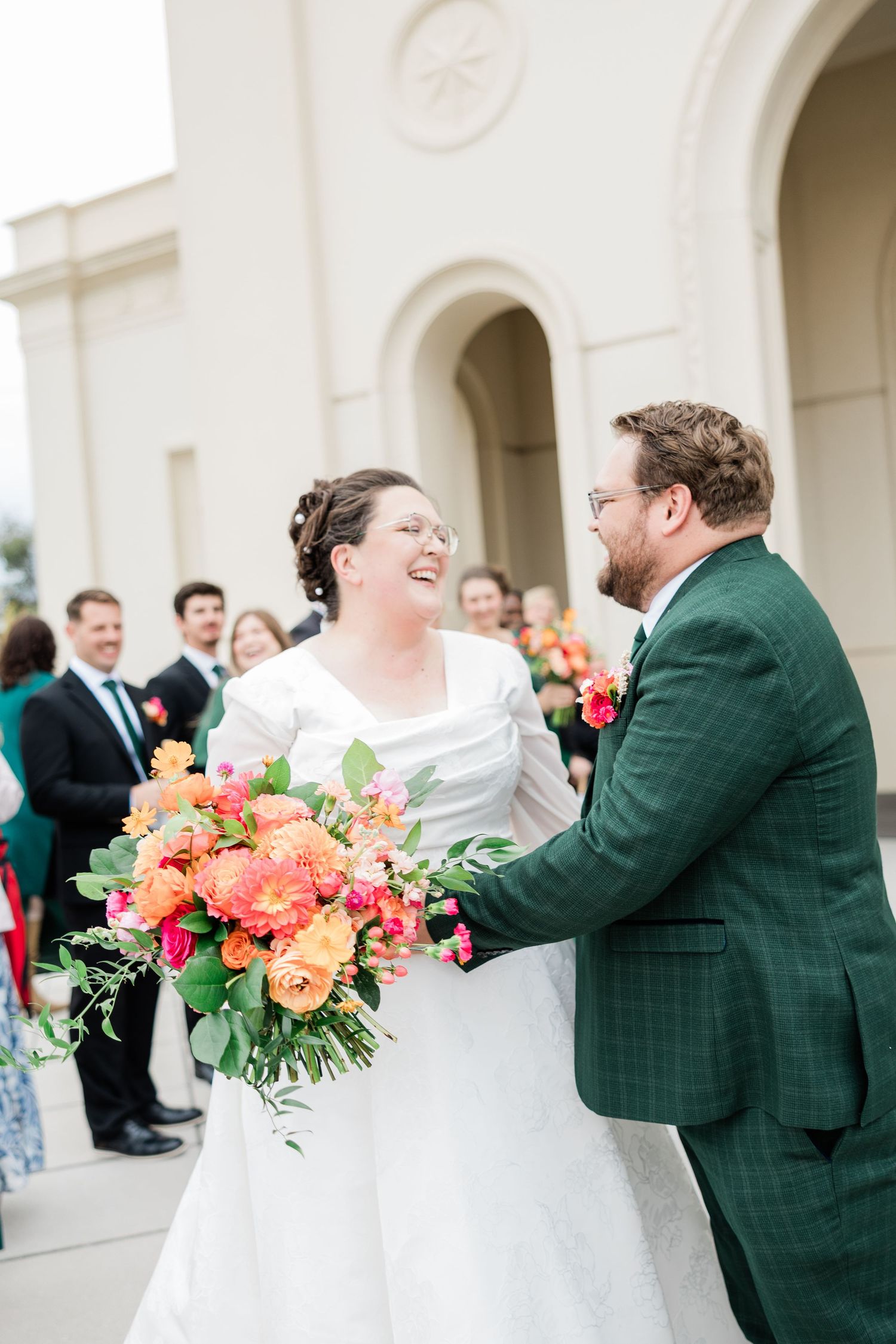 Bride in white dress and groom in green plaid suit share joyful moments with colorful bouquet.