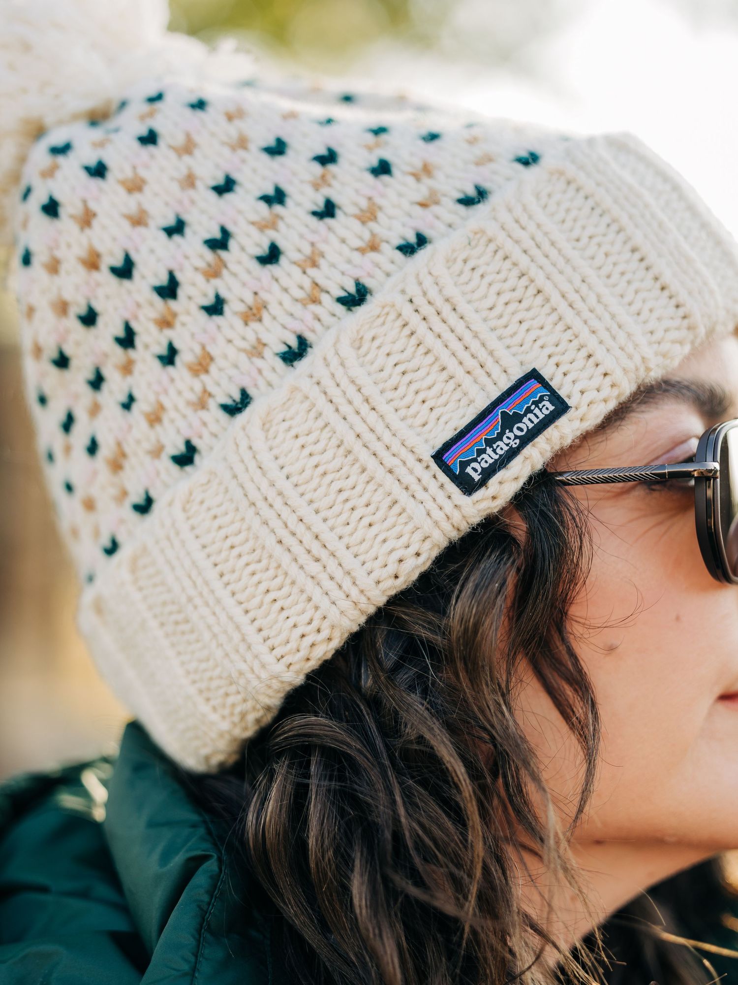 Woman wearing a cream Patagonia knit beanie with colorful pattern and sunglasses outdoors.