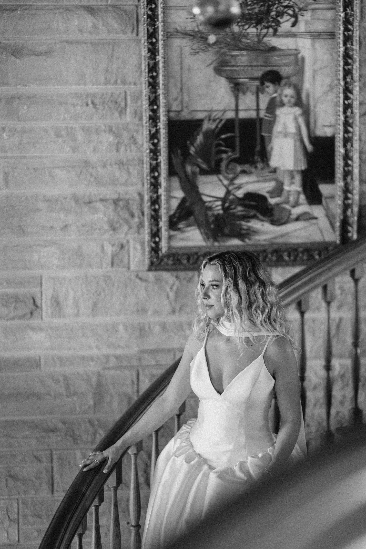 A bride in a white V-neck dress poses elegantly against a stone wall.