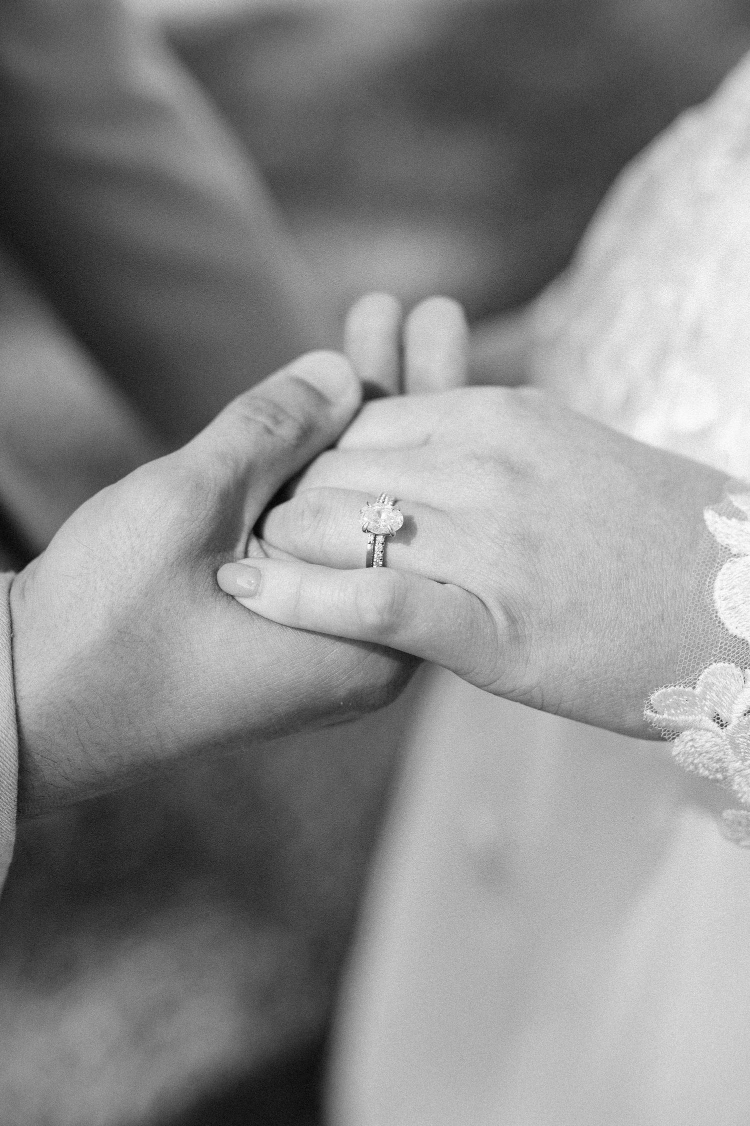 Close-up of hands holding each other in a line showing wedding rings and lace details.