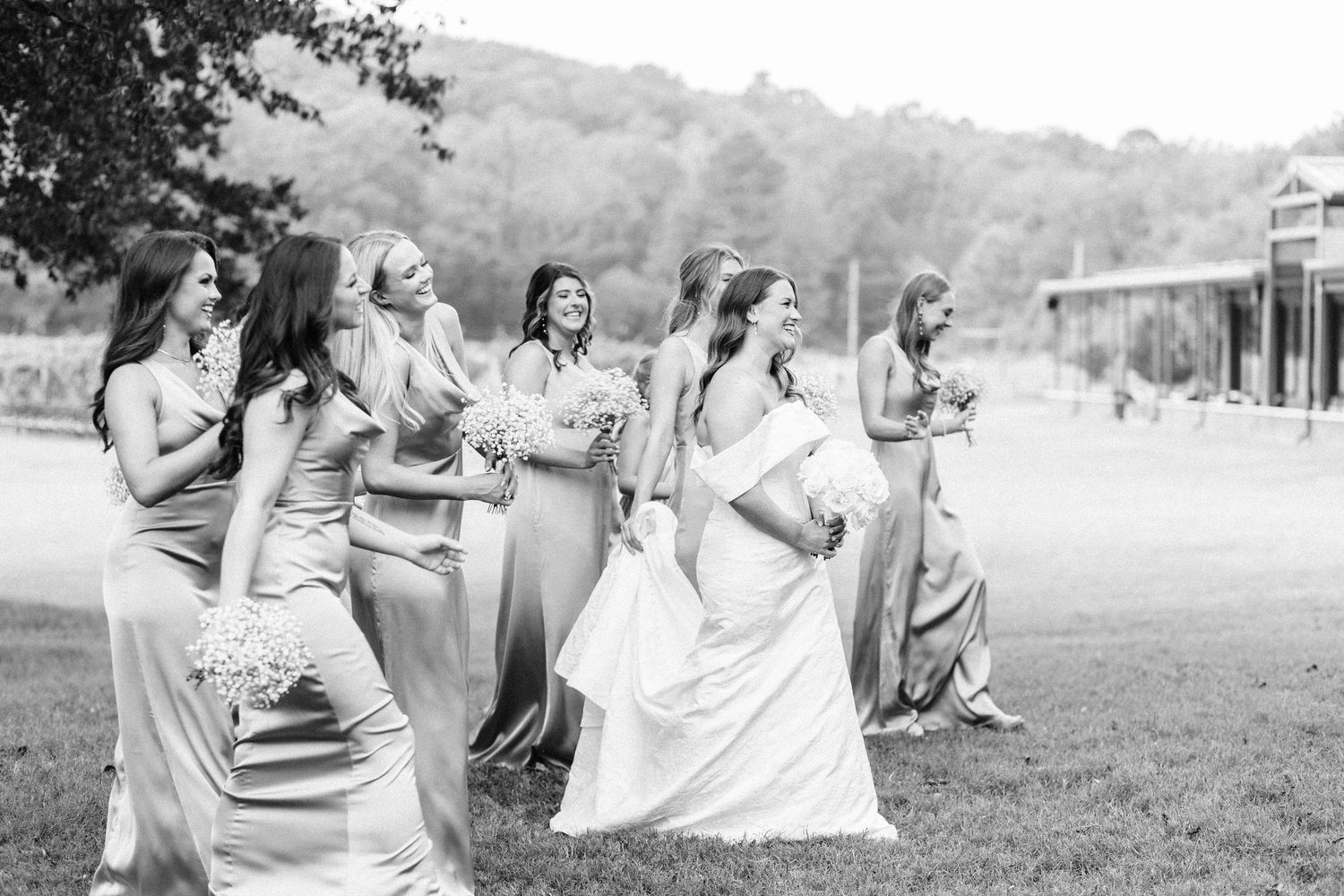 Wedding party members dance and celebrate together on a grassy outdoor venue during a summer celebration.