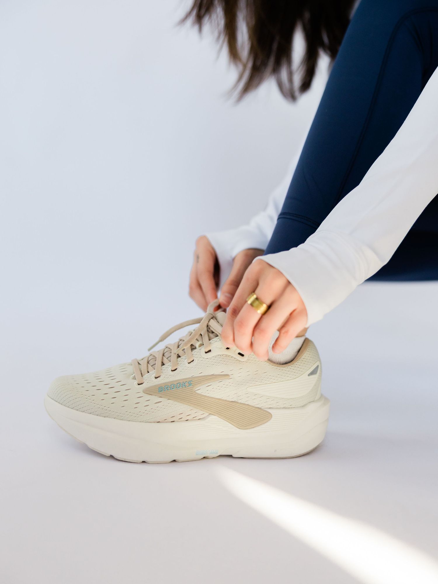 Close-up view of hands tying laces on cream-colored athletic sneakers against a white background.